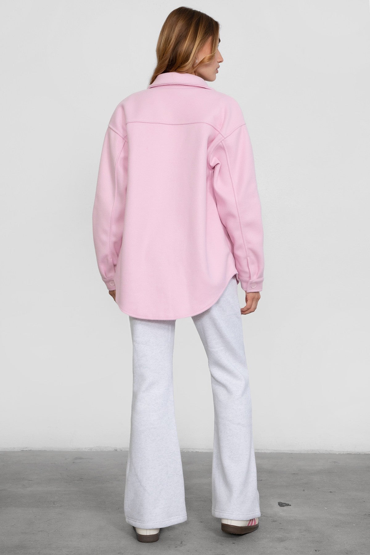 Woman wearing TIC TOC PH29142 JIYA essential fleece flare sweatpants with mid-rise waistband and side pockets from plush fleece collection in heather white paired with a pink jacket.