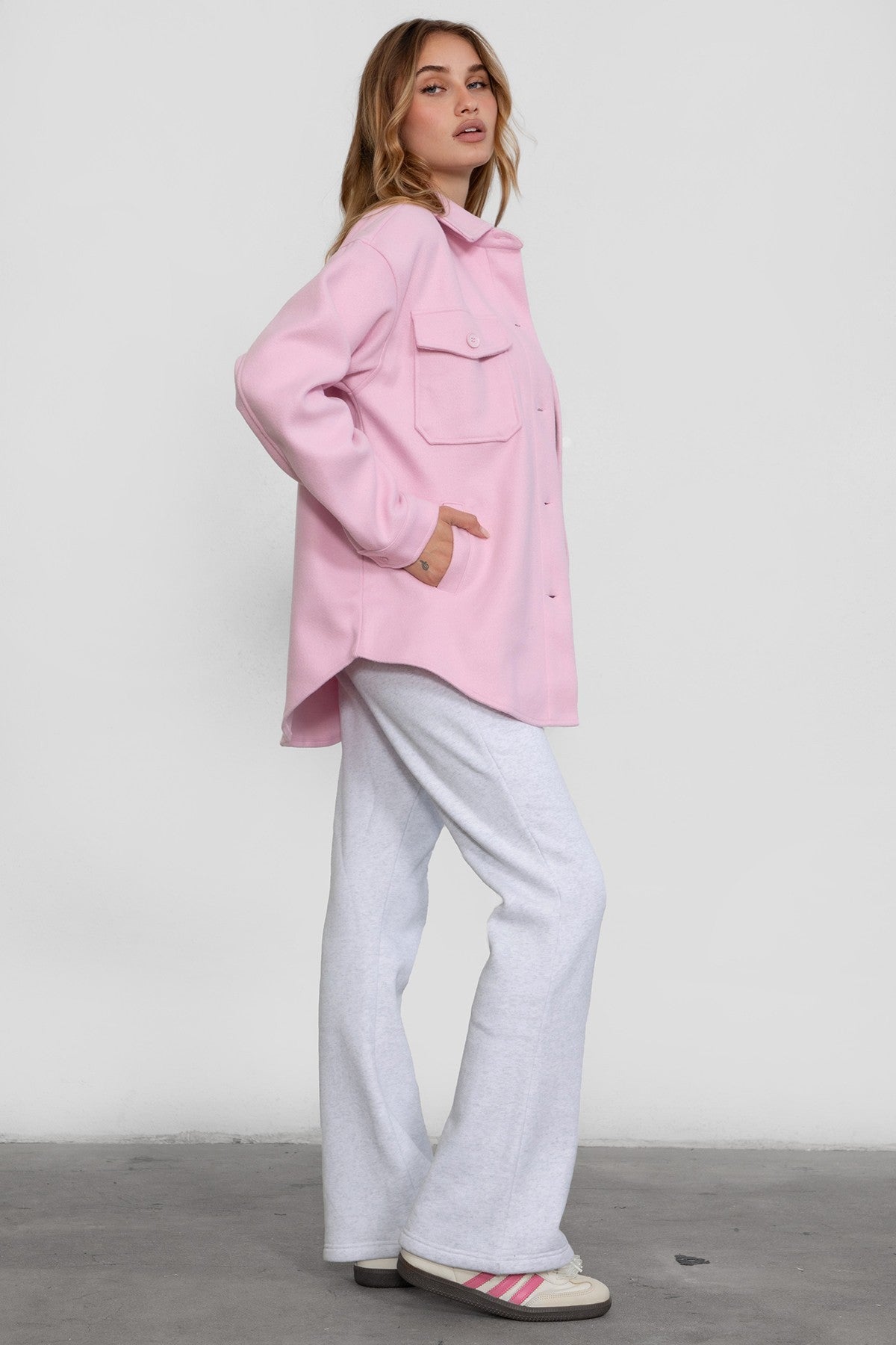 Woman wearing TIC TOC PH29142 JIYA essential fleece flare sweatpants with mid-rise waistband and side pockets from plush fleece collection in heather white paired with a pink jacket.