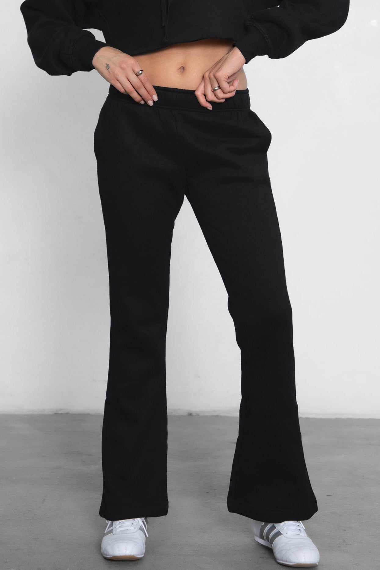 Woman wearing TIC TOC PH29142 JIYA essential fleece flare sweatpants with mid-rise waistband and side pockets from plush fleece collection in black paired with a raw cut matching hoodie.