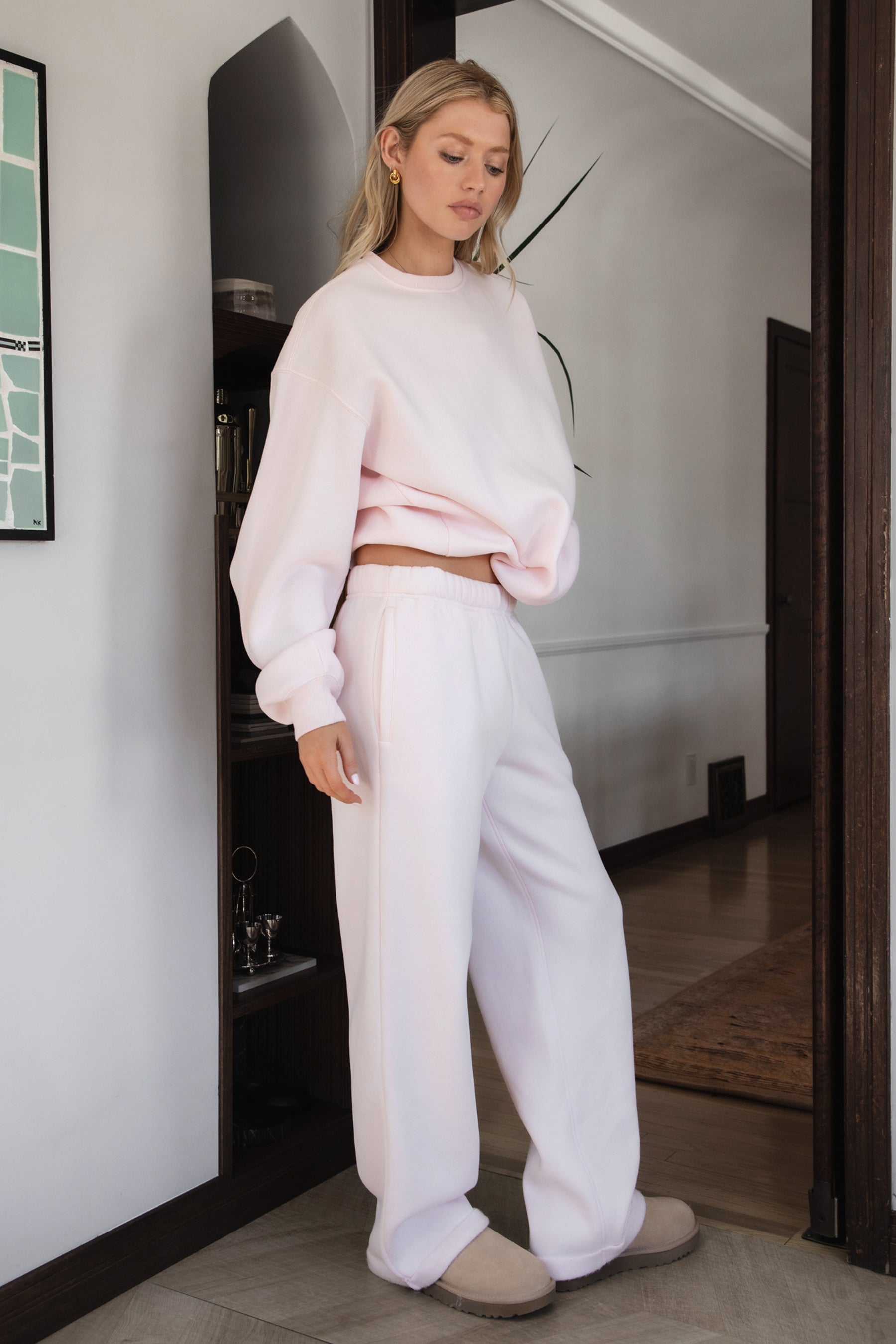 Person wearing a light pink sweater and pants with beige slippers indoors.