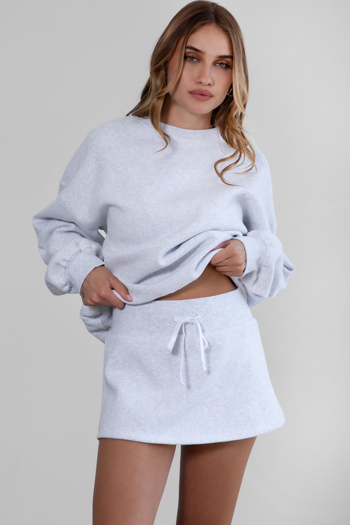 Woman wearing the TIC TOC SH30133BA JEMMA ash fleece mini skirt featuring an elastic waistband, drawstring closure, and hidden shorts for comfort and coverage paired with a matching top.