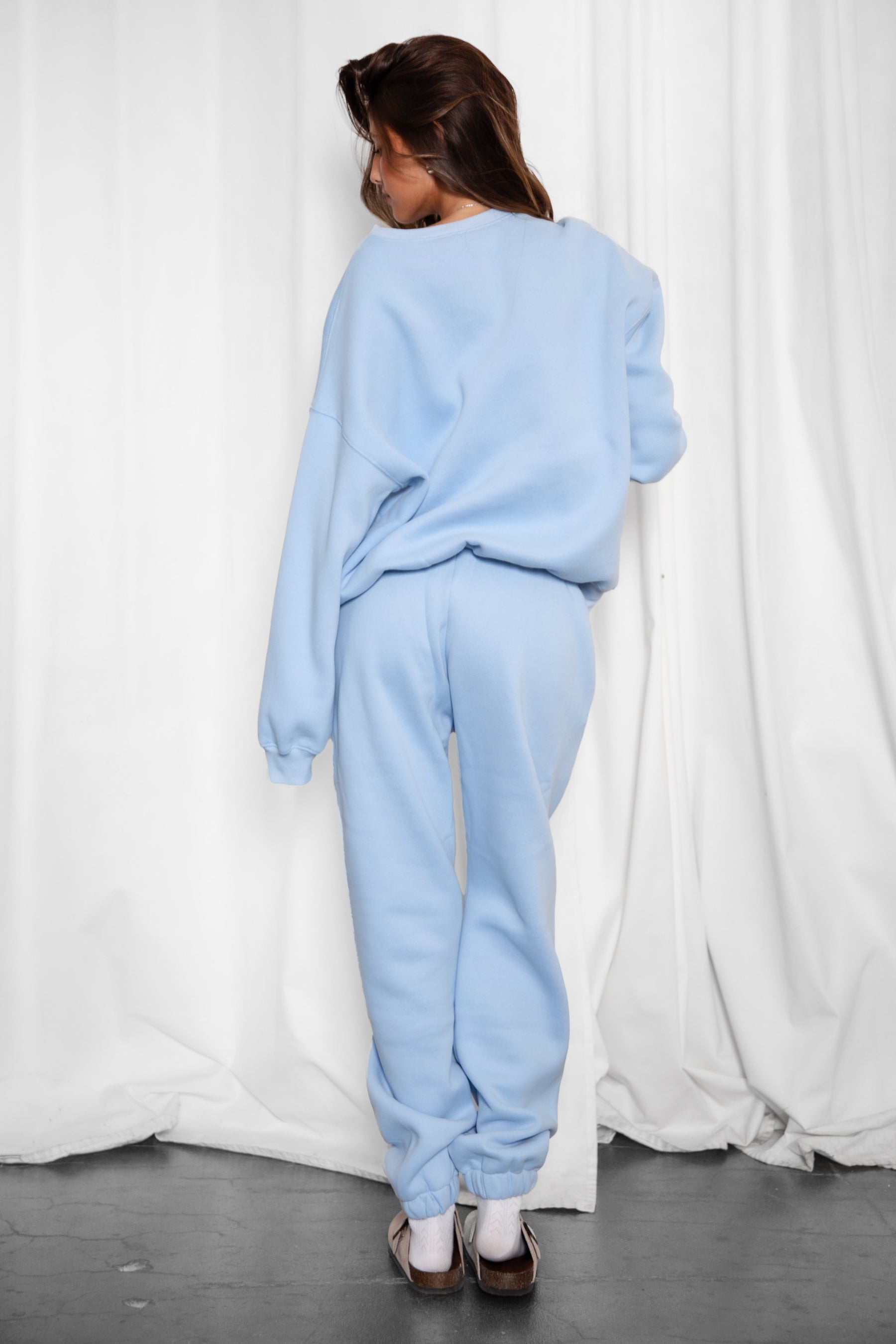 Woman wearing the TIC TOC TH28243 VARSITY baby blue fleece crew neck pullover sweatshirt featuring dropped shoulders, ribbed trim, and plush fleece fabric with the matching bottoms