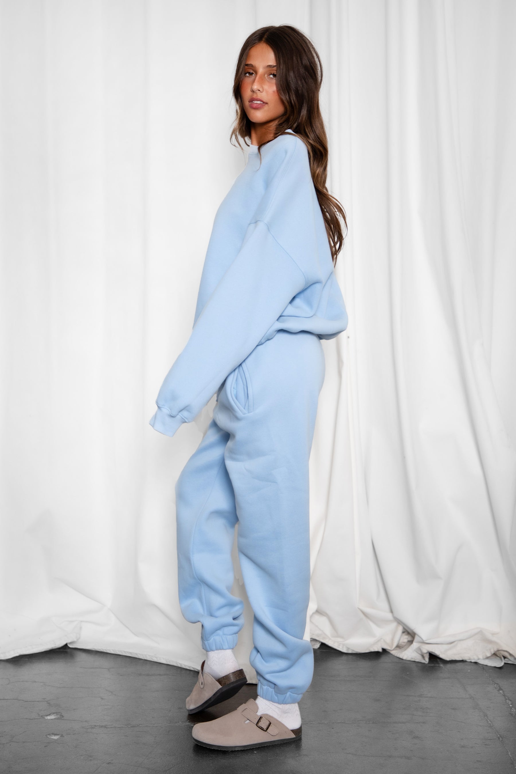 Woman wearing the TIC TOC TH28243 VARSITY baby blue fleece crew neck pullover sweatshirt featuring dropped shoulders, ribbed trim, and plush fleece fabric with the matching bottoms