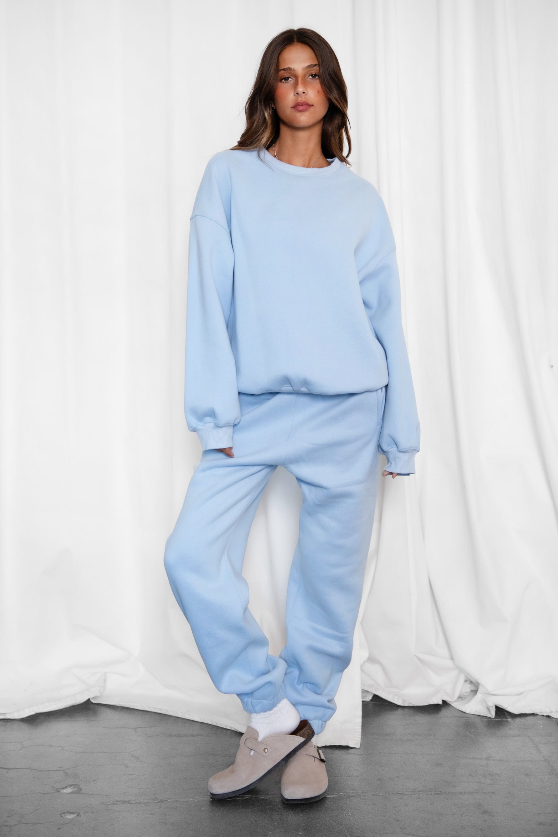 Woman wearing the TIC TOC TH28243 VARSITY baby blue fleece crew neck pullover sweatshirt featuring dropped shoulders, ribbed trim, and plush fleece fabric with the matching bottoms
