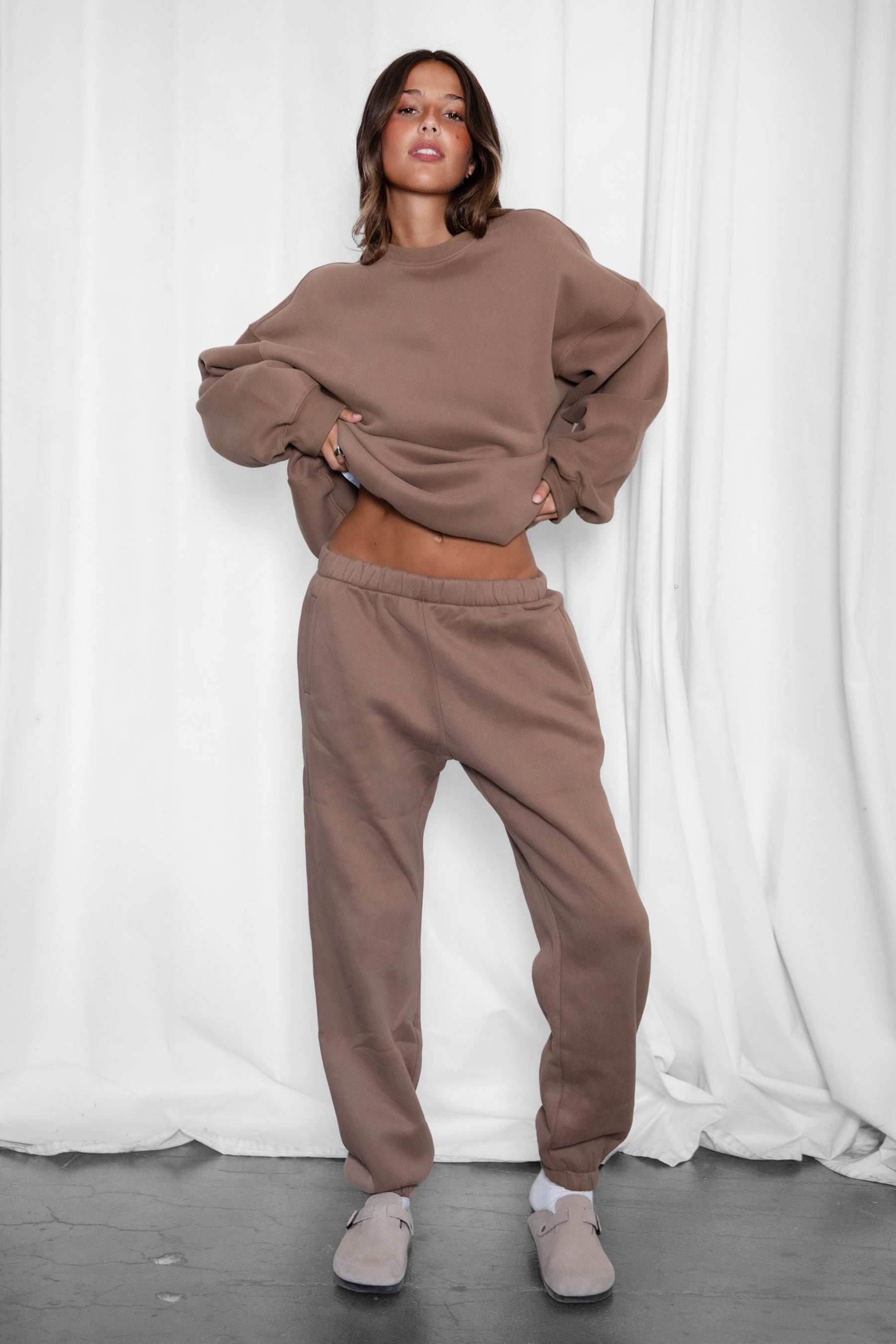 Woman wearing the TIC TOC TH28243 VARSITY coffee fleece crew neck pullover sweatshirt featuring dropped shoulders, ribbed trim, and plush fleece fabric with the matching bottoms