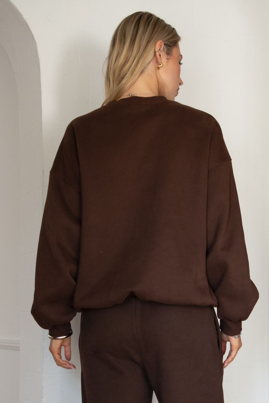 Woman wearing the TIC TOC TH28243 VARSITY brown fleece crew neck pullover sweatshirt featuring dropped shoulders, ribbed trim, and plush fleece fabric with the matching bottoms
