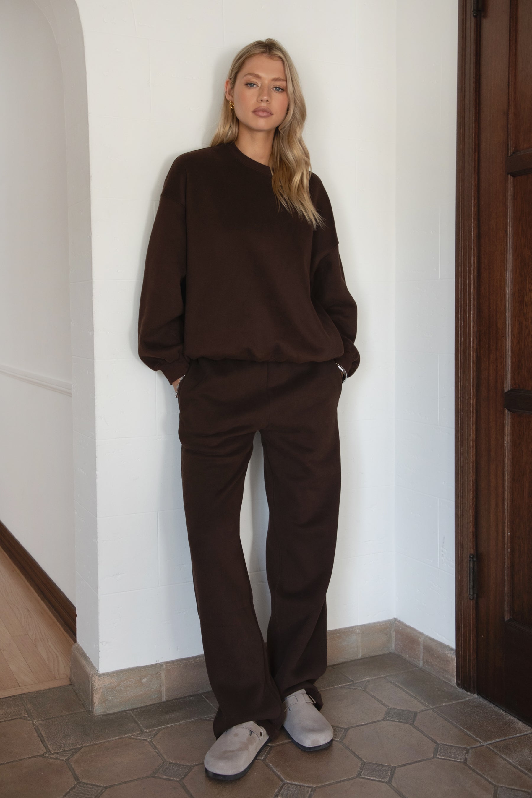 Woman wearing the TIC TOC TH28243 VARSITY brown fleece crew neck pullover sweatshirt featuring dropped shoulders, ribbed trim, and plush fleece fabric with the matching bottoms
