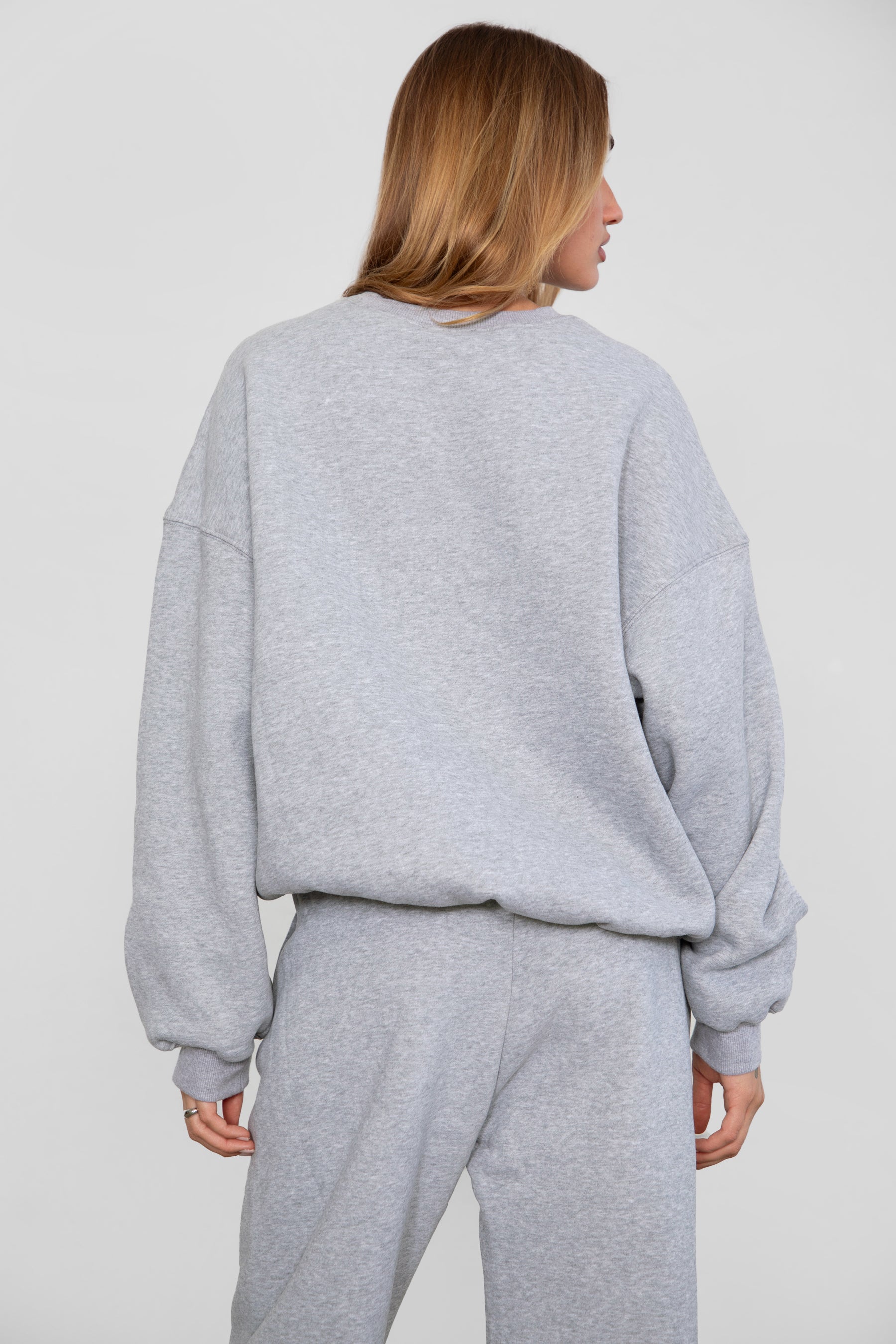 Woman wearing the TIC TOC TH28243 VARSITY heather grey fleece crew neck pullover sweatshirt featuring dropped shoulders, ribbed trim, and plush fleece fabric with the matching bottoms