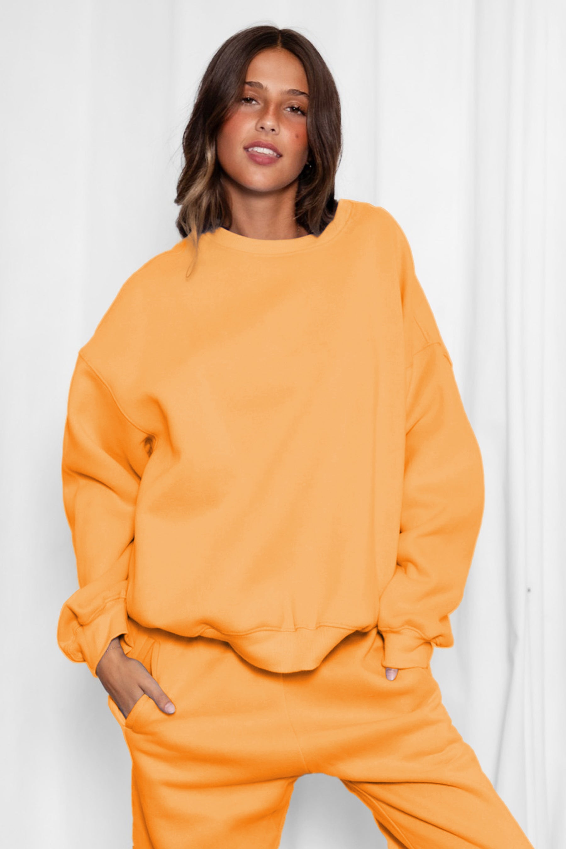 Woman wearing the TIC TOC TH28243 VARSITY orange fleece crew neck pullover sweatshirt featuring dropped shoulders, ribbed trim, and plush fleece fabric with the matching bottoms
