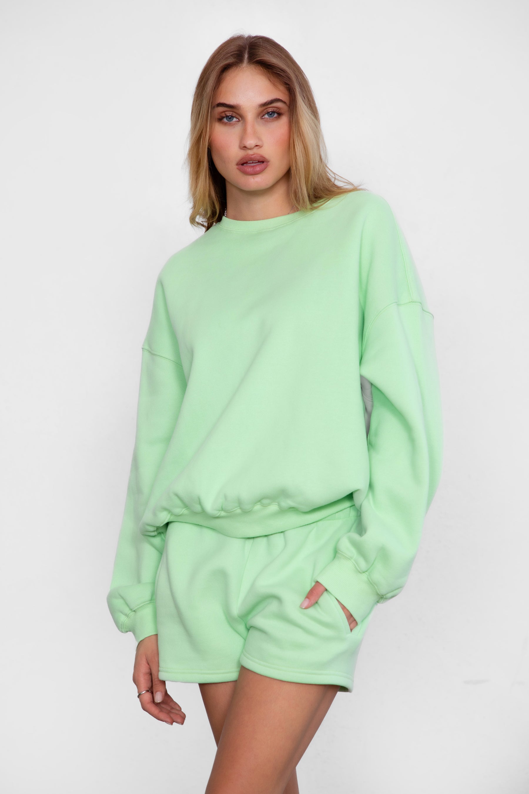 Woman wearing the TIC TOC TH28243 VARSITY pastel lime fleece crew neck pullover sweatshirt featuring dropped shoulders, ribbed trim, and plush fleece fabric with the matching bottoms