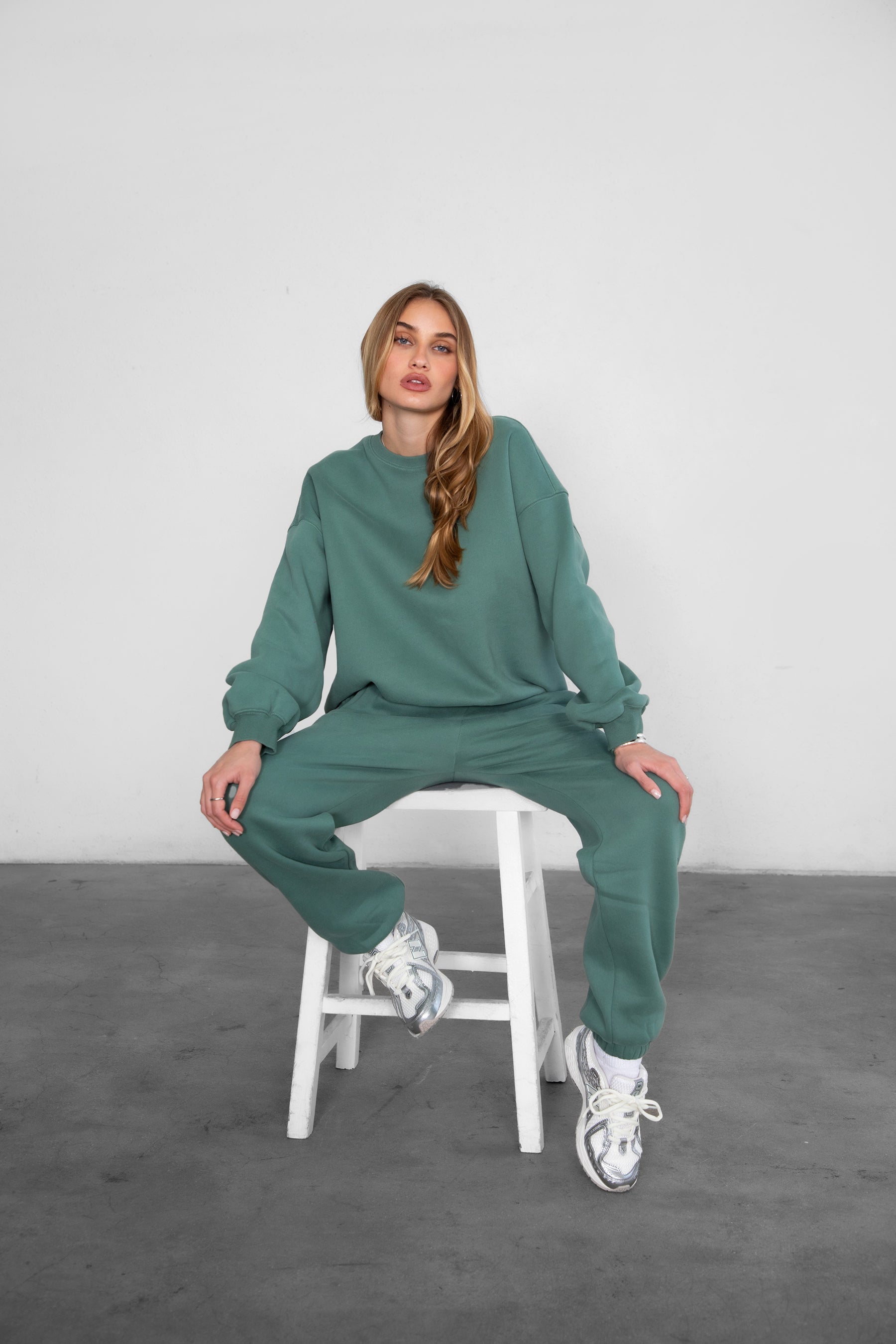 Woman wearing the TIC TOC TH28243 VARSITY pine green fleece crew neck pullover sweatshirt featuring dropped shoulders, ribbed trim, and plush fleece fabric with the matching bottoms