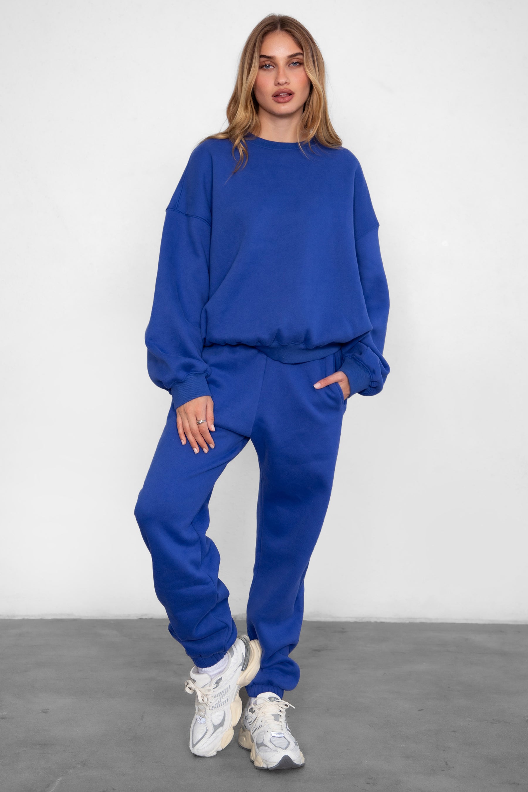 Woman wearing the TIC TOC TH28243 VARSITY royal blue fleece crew neck pullover sweatshirt featuring dropped shoulders, ribbed trim, and plush fleece fabric with the matching bottoms