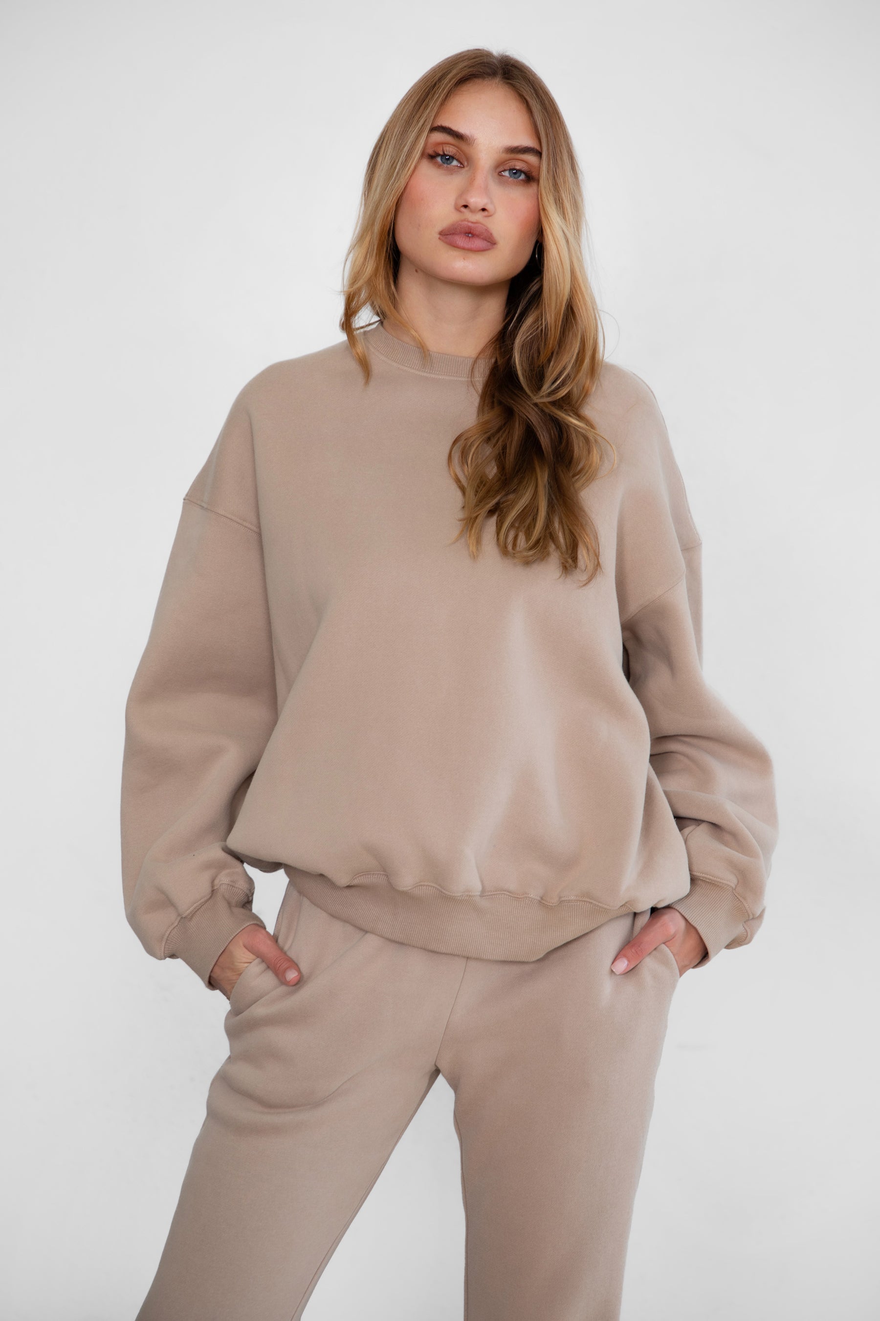 Woman wearing the TIC TOC TH28243 VARSITY taupe fleece crew neck pullover sweatshirt featuring dropped shoulders, ribbed trim, and plush fleece fabric with the matching bottoms