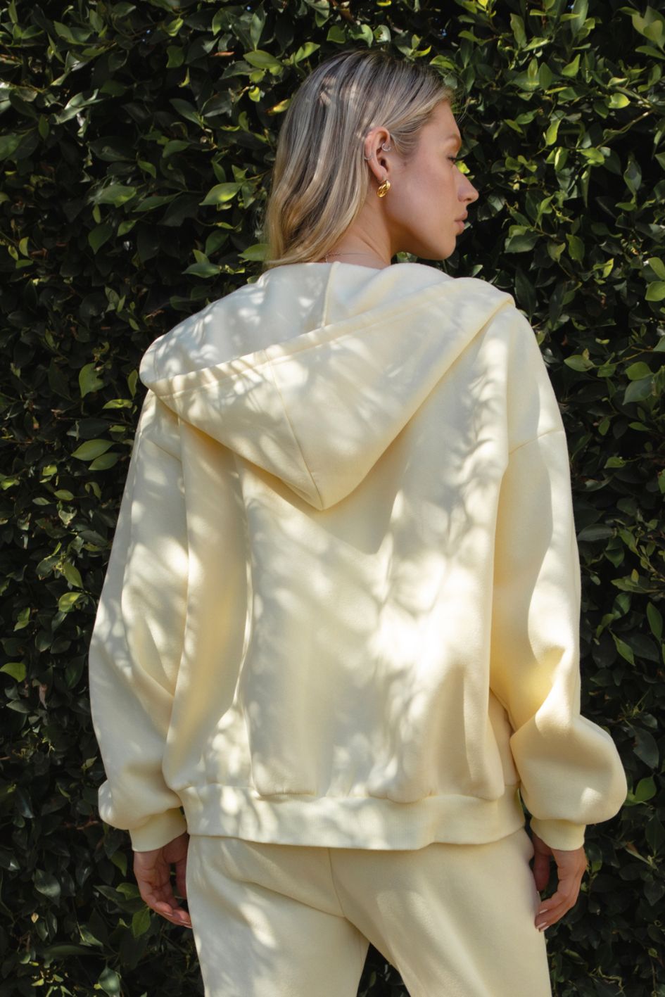 Woman wearing the TIC TOC TH29489 UNIVERSITY pale yellow oversized loose fit zip up hoodie featuring dropped shoulders, ribbed hem, and plush fleece fabric with matching bottoms.