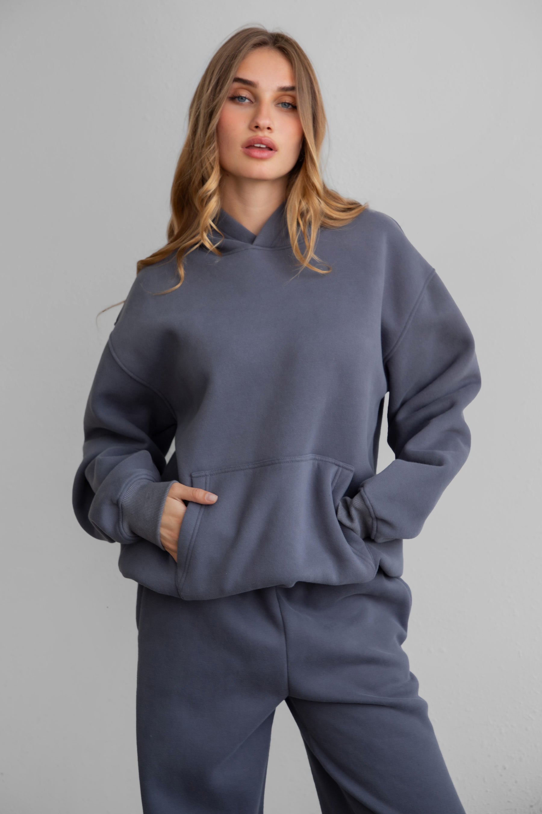 A female model wearing a steel grey oversized hoodie with a hood, long sleeves paired with matching bottoms.