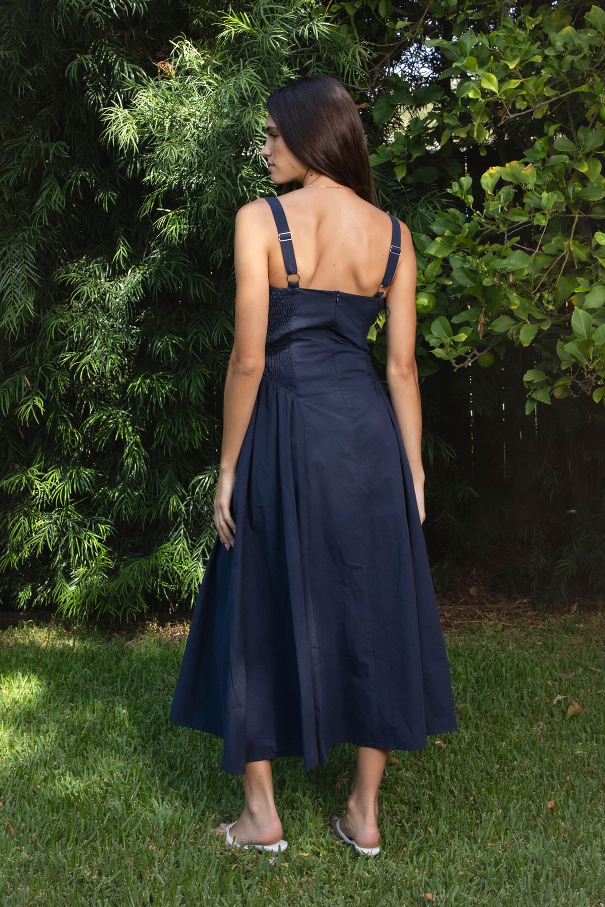 Woman wearing NAVYA scoop neck cotton poplin midi dress featuring soft smooth cotton poplin fabric, feminine scoop neckline with delicate picot trim, wide shoulder straps with adjustable back detail, gathered bust with built in bra cups, fitted waistline with shaped seam detailing, smocked back panel, and full flared midi length skirt with soft side gathers and rayon lining.