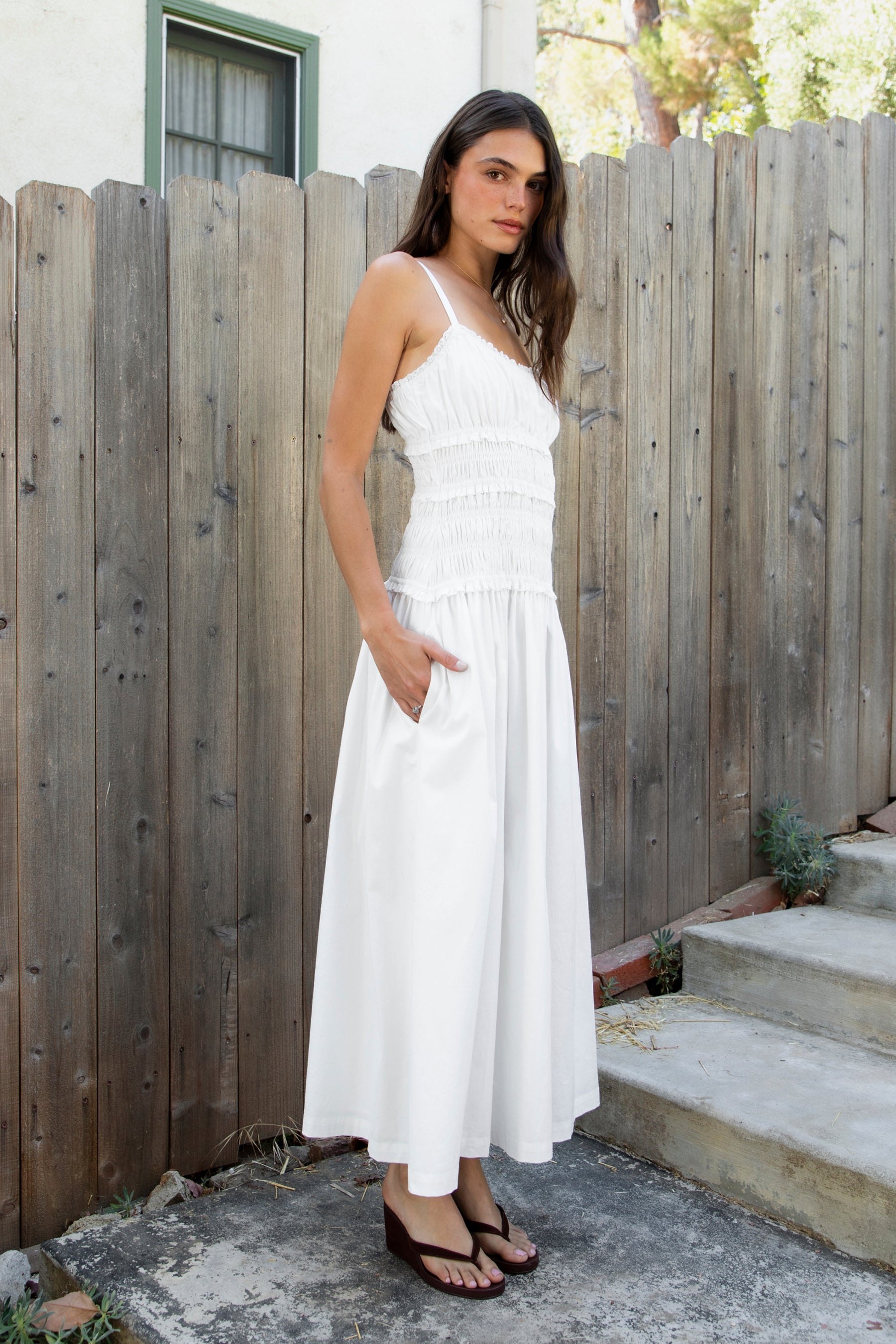 Woman wearing ISLA smocked poplin square neck maxi dress featuring smooth stretch poplin fabric, built in bra cups, straight neckline with ruffle detail, adjustable spaghetti straps, fully smocked bodice, flowing maxi skirt, hidden side pockets, and easy pull on design.