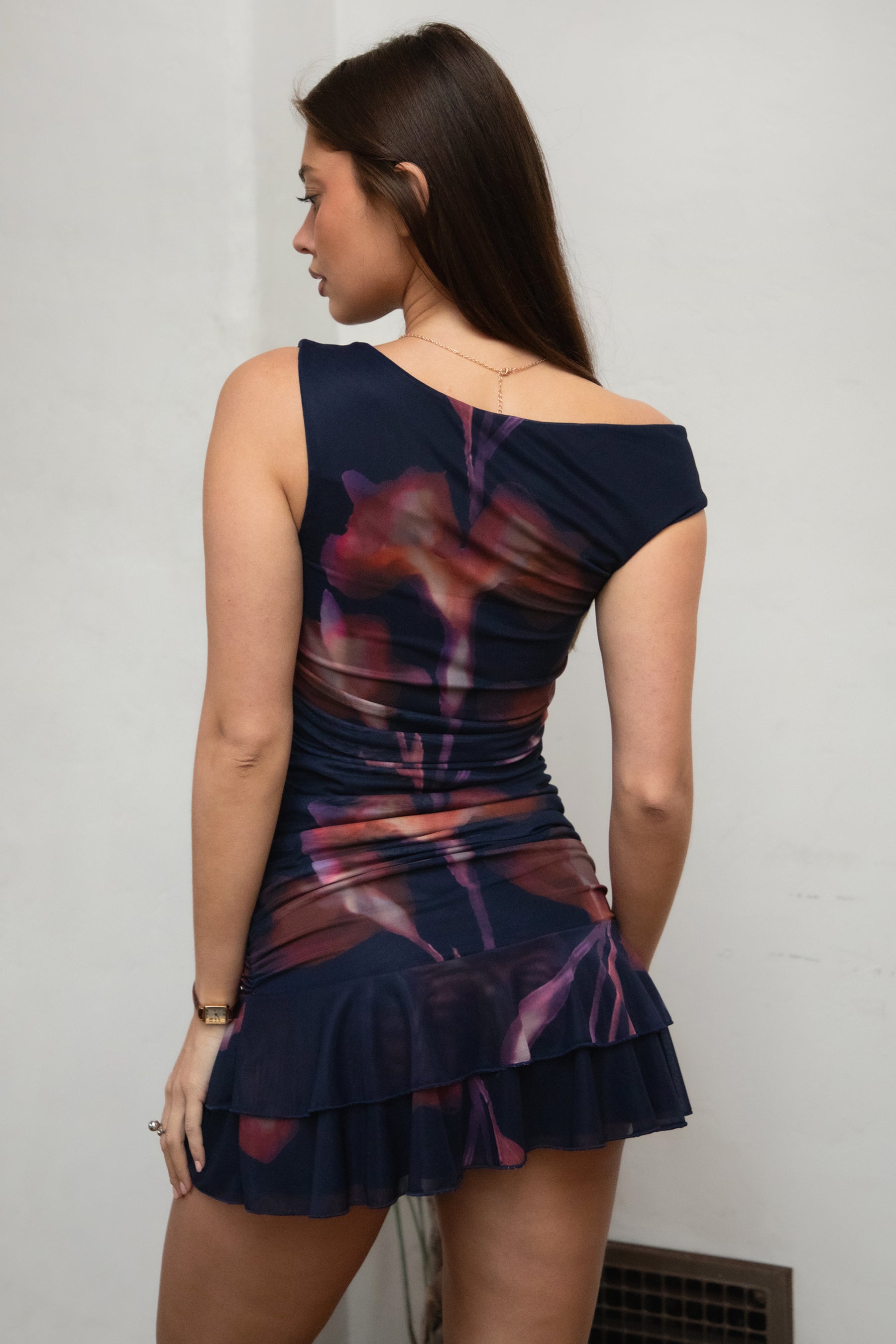 Woman wearing TIC TOC DC31652-VIORELLE VIORELLE mini dress featuring a twisted one-shoulder mesh silhouette with bold graphic print, ruched side detailing, layered ruffle hem mini skirt, and body-hugging fit with a lightweight sheer overlay, styled for a night-out look with heels and minimal accessories.