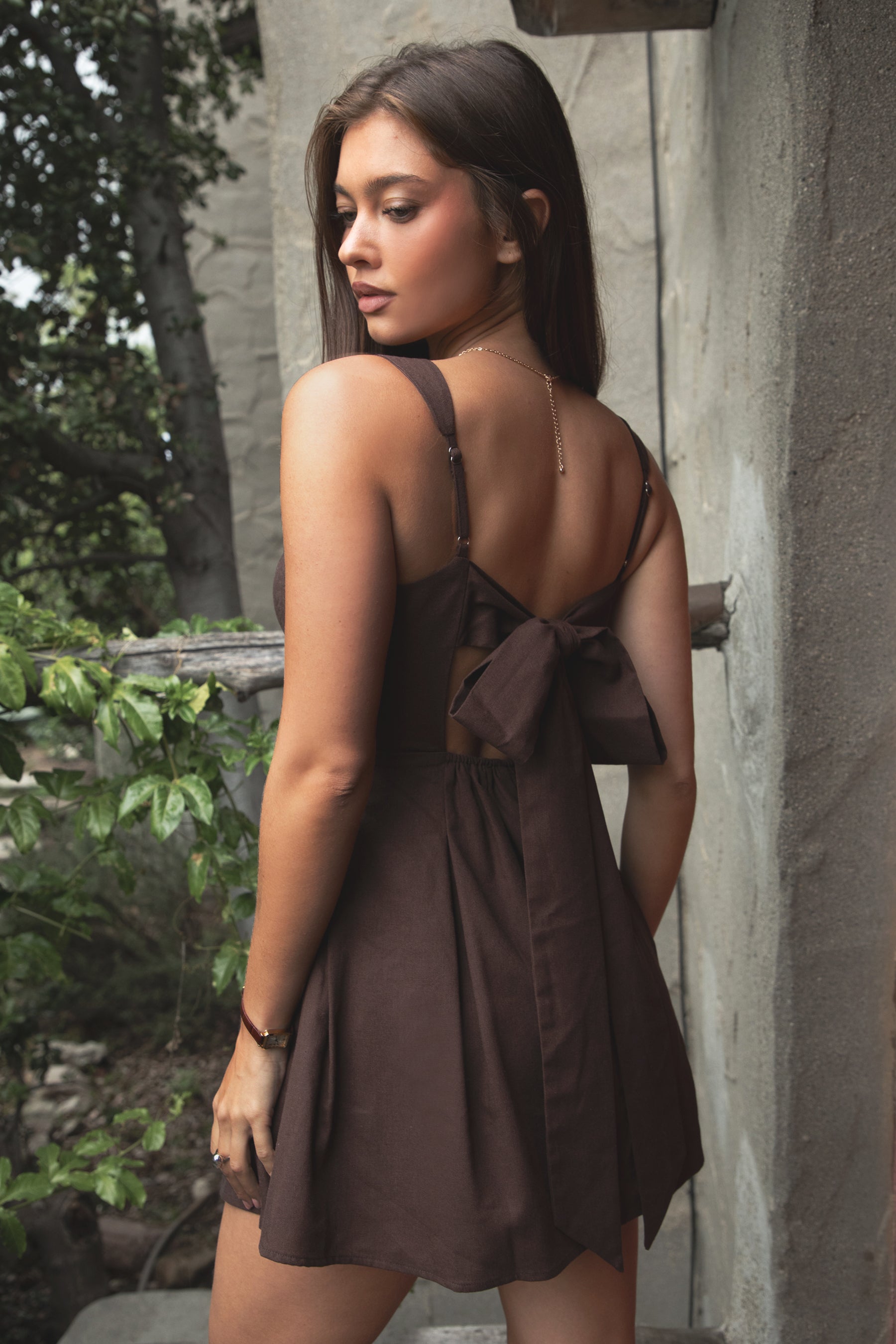 Woman wearing TIC TOC DH31916-ZENAYA ZENAYA mini dress featuring a fit-and-flare mini silhouette, clean square neckline, adjustable wide shoulder straps, shaped bust seams, and a bow tie open back detail, with soft linen-blend drape and lightweight structure styled for a summer-ready brunch or garden party look.