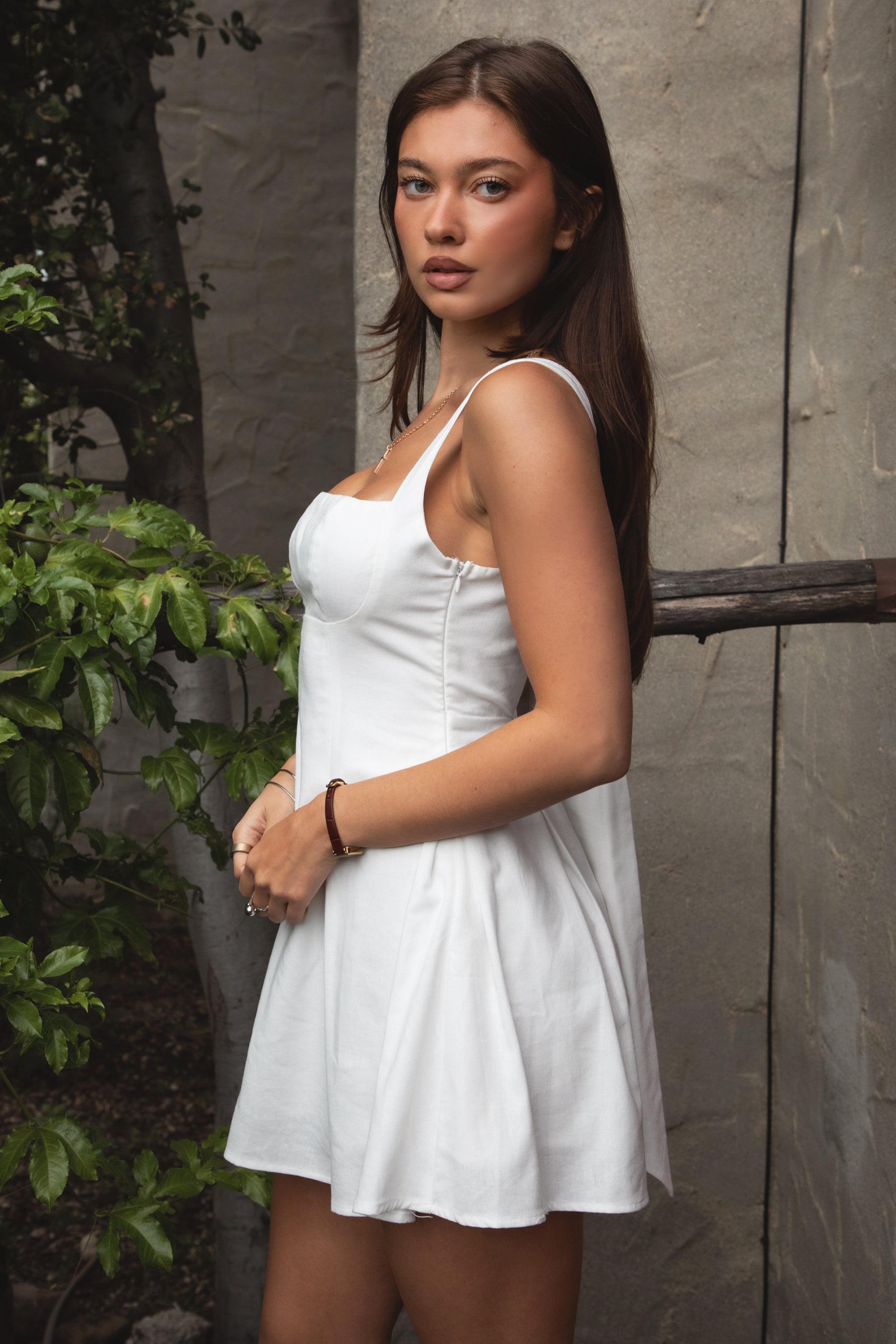 Woman wearing TIC TOC DH31916-ZENAYA ZENAYA mini dress featuring a fit-and-flare mini silhouette, clean square neckline, adjustable wide shoulder straps, shaped bust seams, and a bow tie open back detail, with soft linen-blend drape and lightweight structure styled for a summer-ready brunch or garden party look.