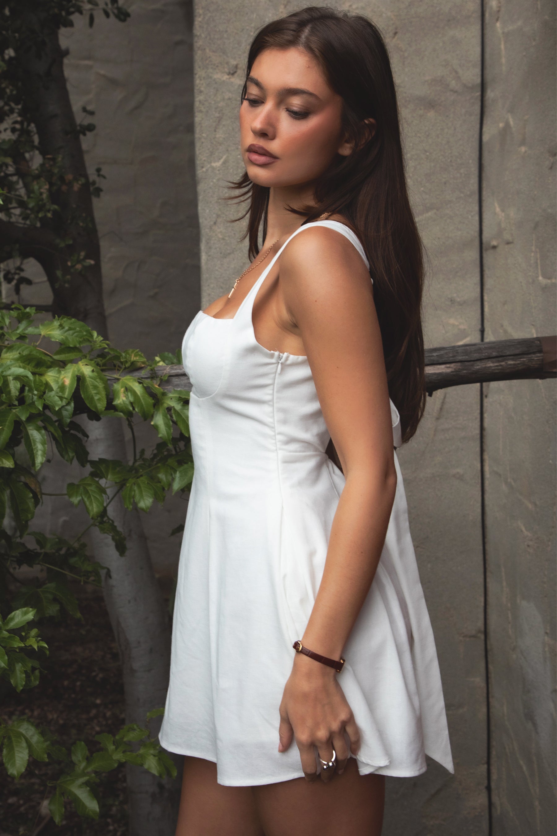 Woman wearing TIC TOC DH31916-ZENAYA ZENAYA mini dress featuring a fit-and-flare mini silhouette, clean square neckline, adjustable wide shoulder straps, shaped bust seams, and a bow tie open back detail, with soft linen-blend drape and lightweight structure styled for a summer-ready brunch or garden party look.