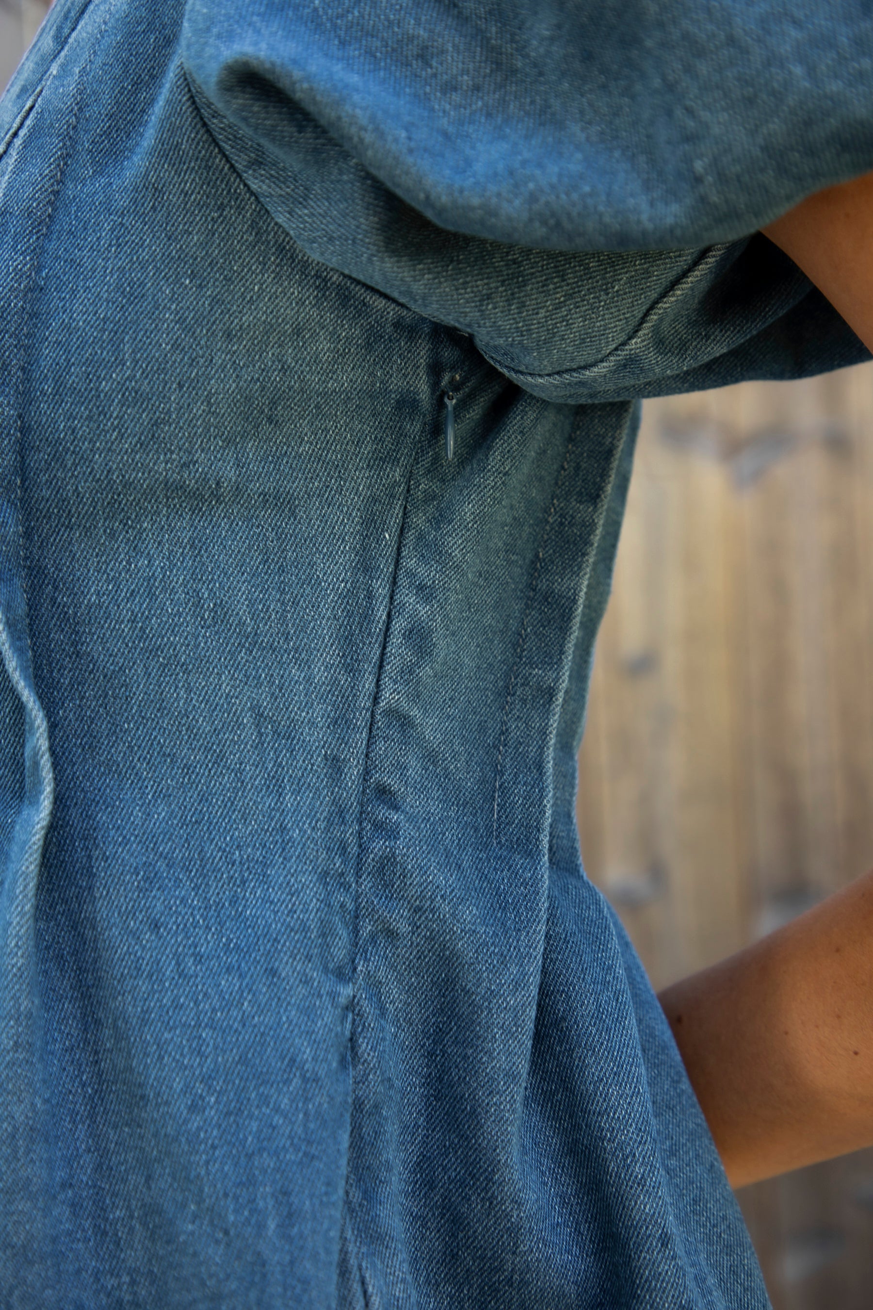 Woman wearing DELANEY soft denim puff sleeve denim romper featuring soft denim fabric, comfortable structured feel, deep V neckline, adjustable front tie detail, statement puff sleeves with gathered volume, pleated bodice, relaxed fit silhouette, and hidden side zipper closure.