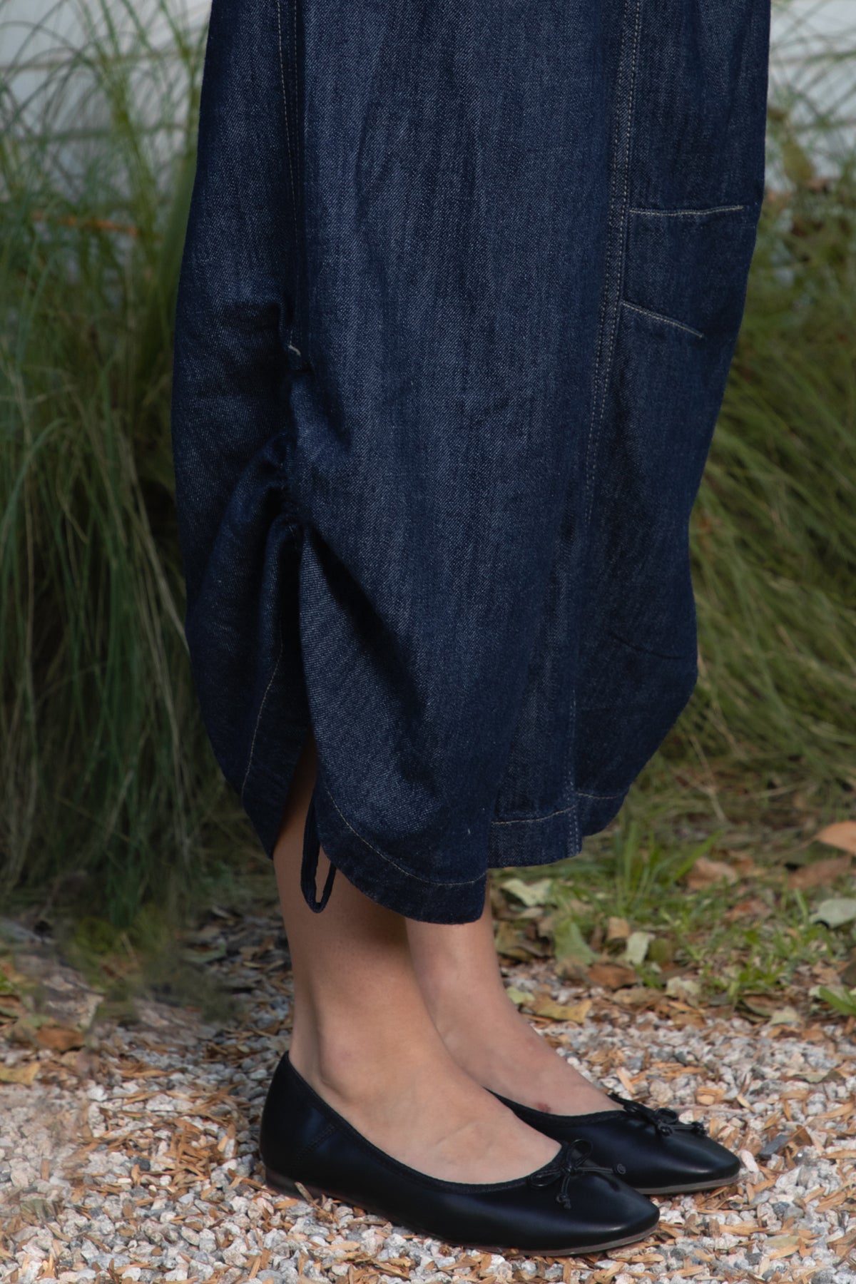 Woman wearing SHILOW ruffle sleeve wide leg denim jumpsuit featuring classic dark blue cotton blend denim fabric, collared neckline with front button closure, feminine gathered ruffle cap sleeves, smocked elastic waistband, front pleated detailing, relaxed balloon leg silhouette with cropped length, adjustable drawstring details at the leg hems, functional side pockets, back patch pockets, and contrast stitching throughout.