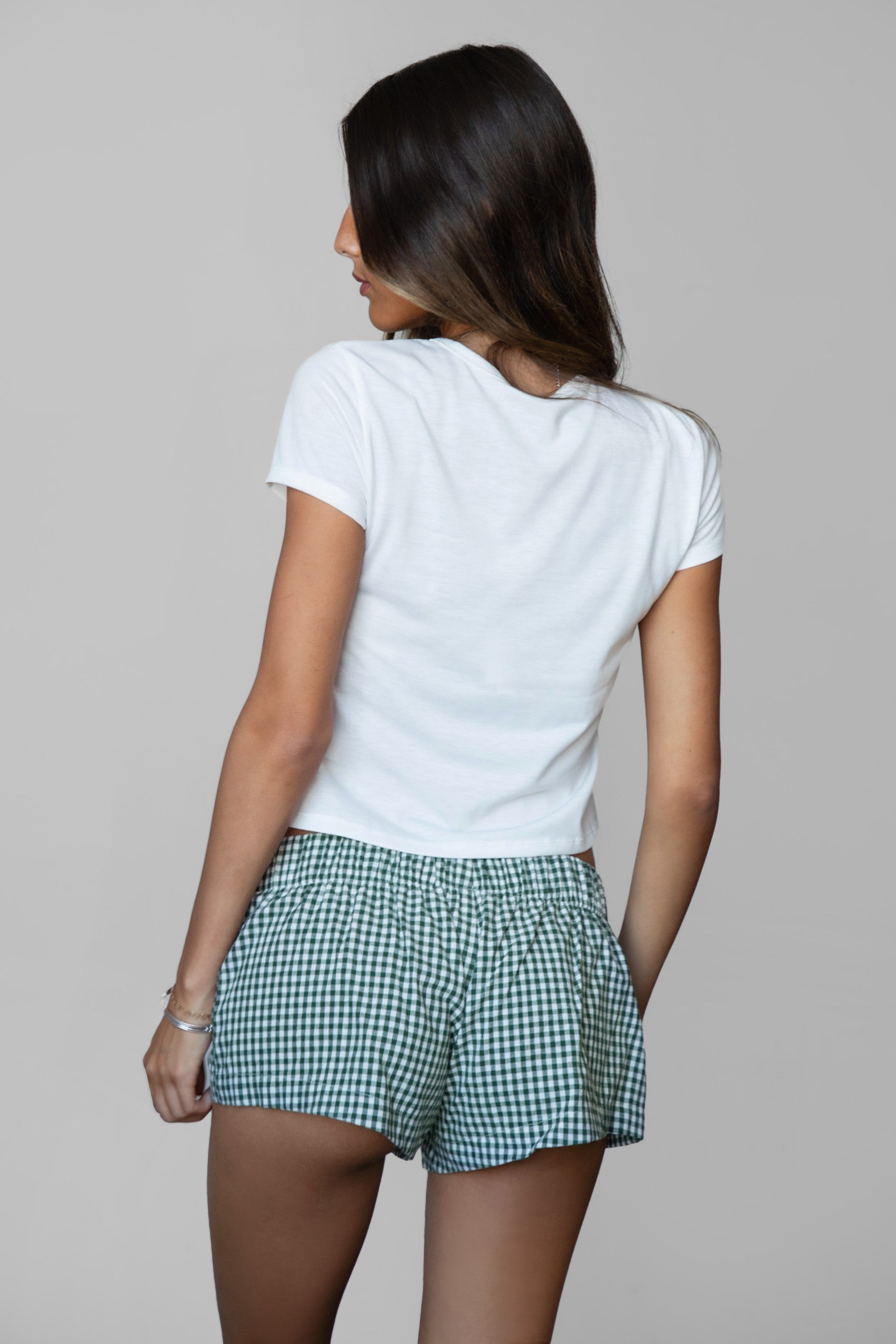 Person wearing a white t-shirt and green checkered shorts on a plain background