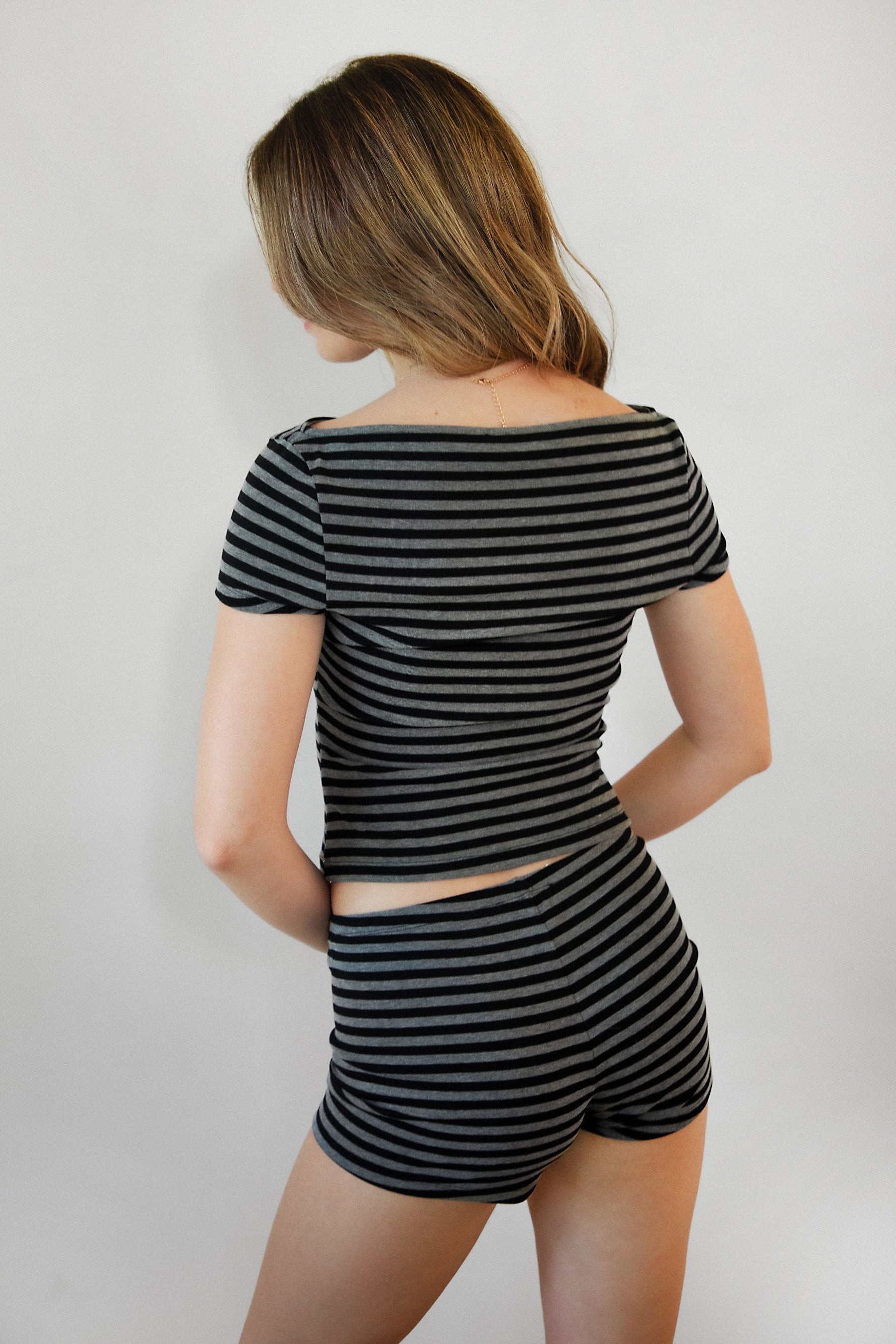 Woman wearing VELA stripe jersey micro shorts featuring a classic stripe print, soft stretch jersey fabric, fitted micro short silhouette, elastic waistband, and lightweight construction designed for lounging, layering, and coordinated matching set styling.