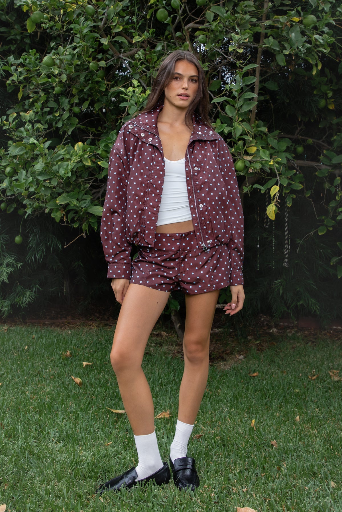 Woman wearing DOLLY polka dot low rise micro shorts featuring smooth lightweight woven polyester fabric, allover contrast polka dot print, low rise waistline, wide structured waistband with belt loops, fitted micro mini silhouette, front seam detailing, hidden front zipper closure, and full polyester lining for comfortable wear.