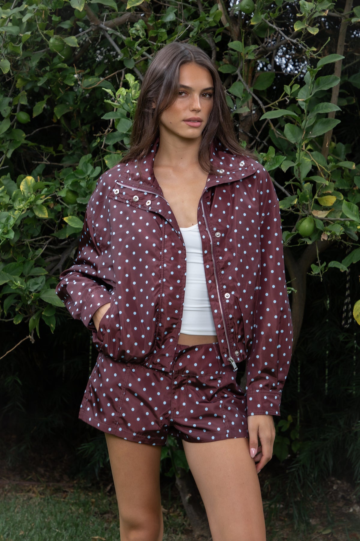 Woman wearing DOLLY polka dot low rise micro shorts featuring smooth lightweight woven polyester fabric, allover contrast polka dot print, low rise waistline, wide structured waistband with belt loops, fitted micro mini silhouette, front seam detailing, hidden front zipper closure, and full polyester lining for comfortable wear.