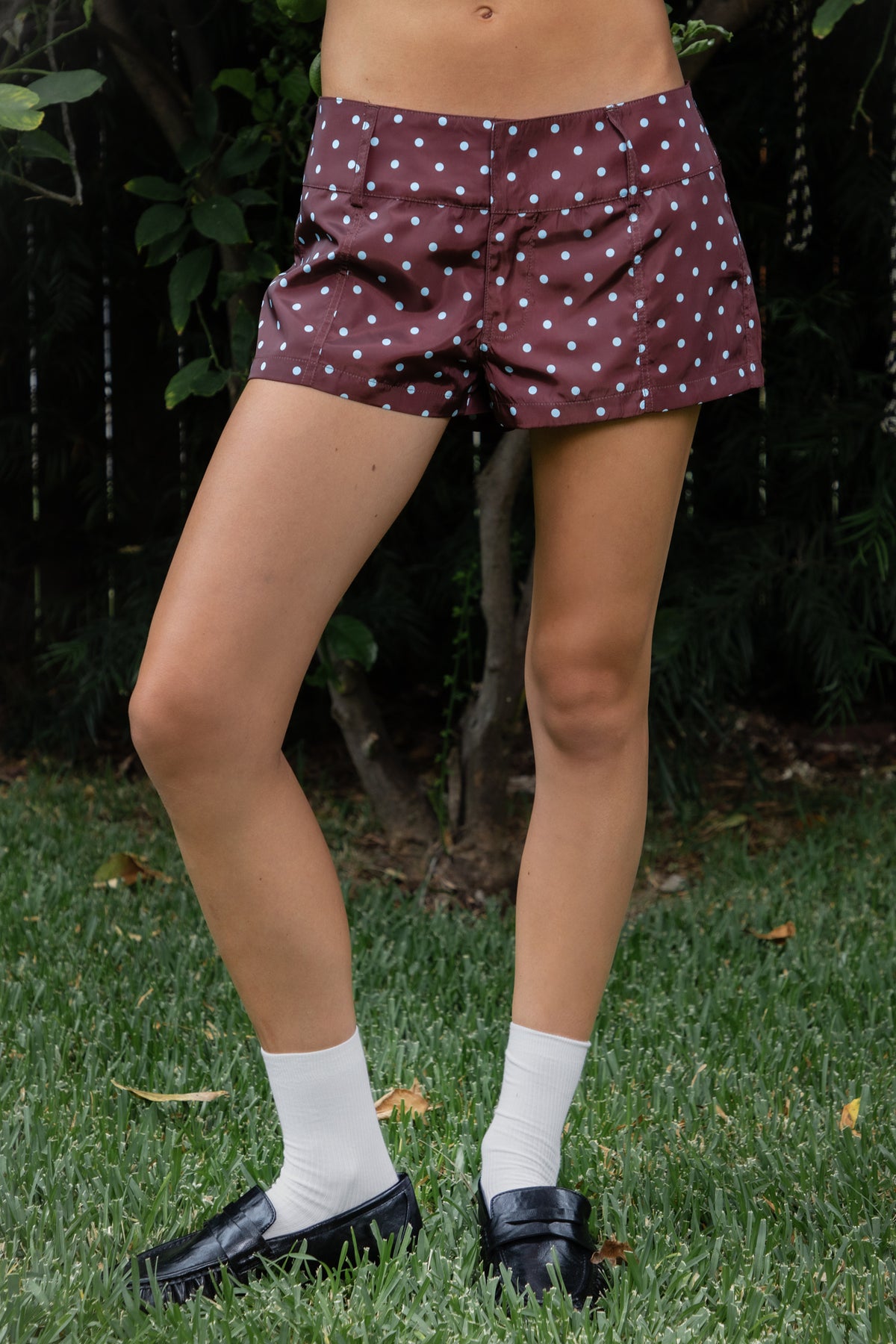 Woman wearing DOLLY polka dot low rise micro shorts featuring smooth lightweight woven polyester fabric, allover contrast polka dot print, low rise waistline, wide structured waistband with belt loops, fitted micro mini silhouette, front seam detailing, hidden front zipper closure, and full polyester lining for comfortable wear.