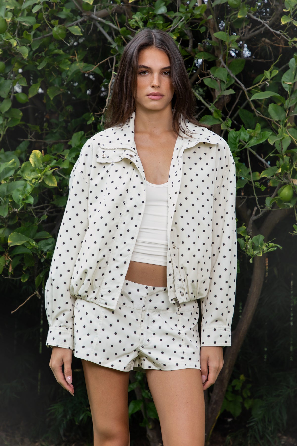 Woman wearing DOLLY polka dot low rise micro shorts featuring smooth lightweight woven polyester fabric, allover contrast polka dot print, low rise waistline, wide structured waistband with belt loops, fitted micro mini silhouette, front seam detailing, hidden front zipper closure, and full polyester lining for comfortable wear.