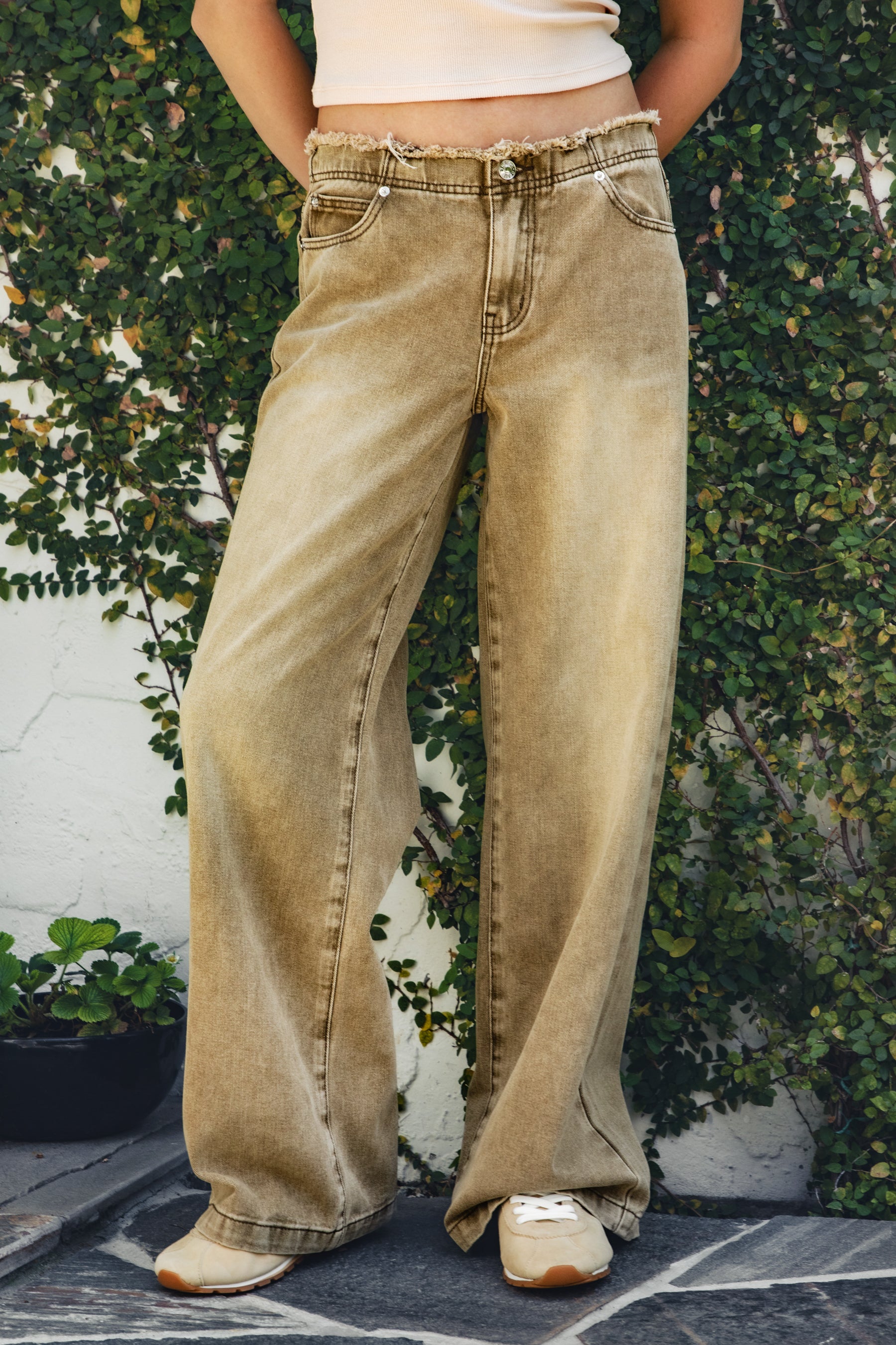 Woman wearing CINDER washed distressed hem wide leg jean featuring a vintage washed denim finish, distressed raw waistband detail, mid rise wide leg silhouette, classic five pocket design, and button and zip front closure for western inspired everyday styling.