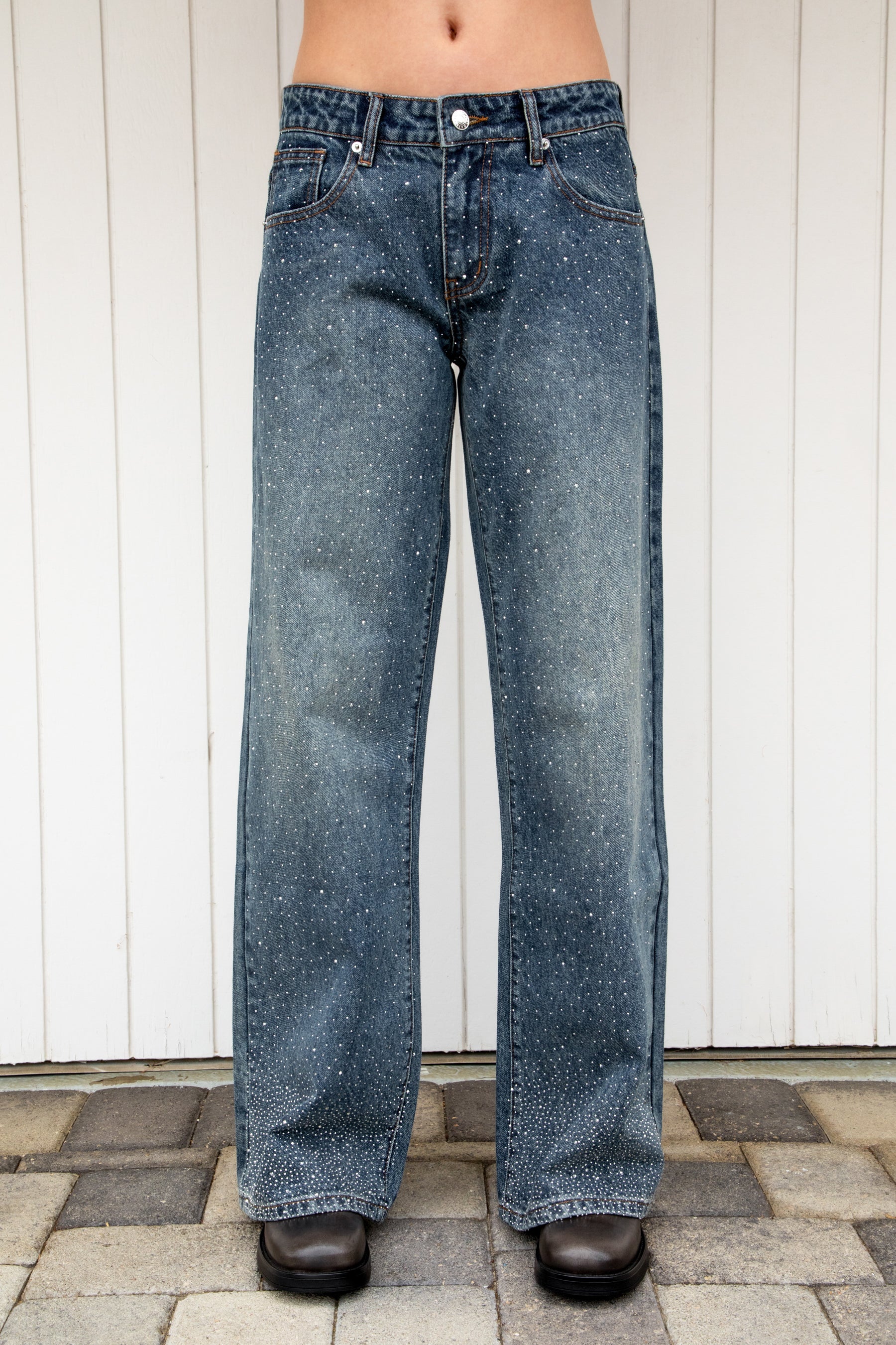 Woman wearing STERLING rhinestone straight leg jean featuring premium cotton denim, allover sparkling rhinestone embellishments, mid rise waist, relaxed straight leg silhouette, subtle vintage wash, classic five pocket design, zip fly, and button closure for statement styling.