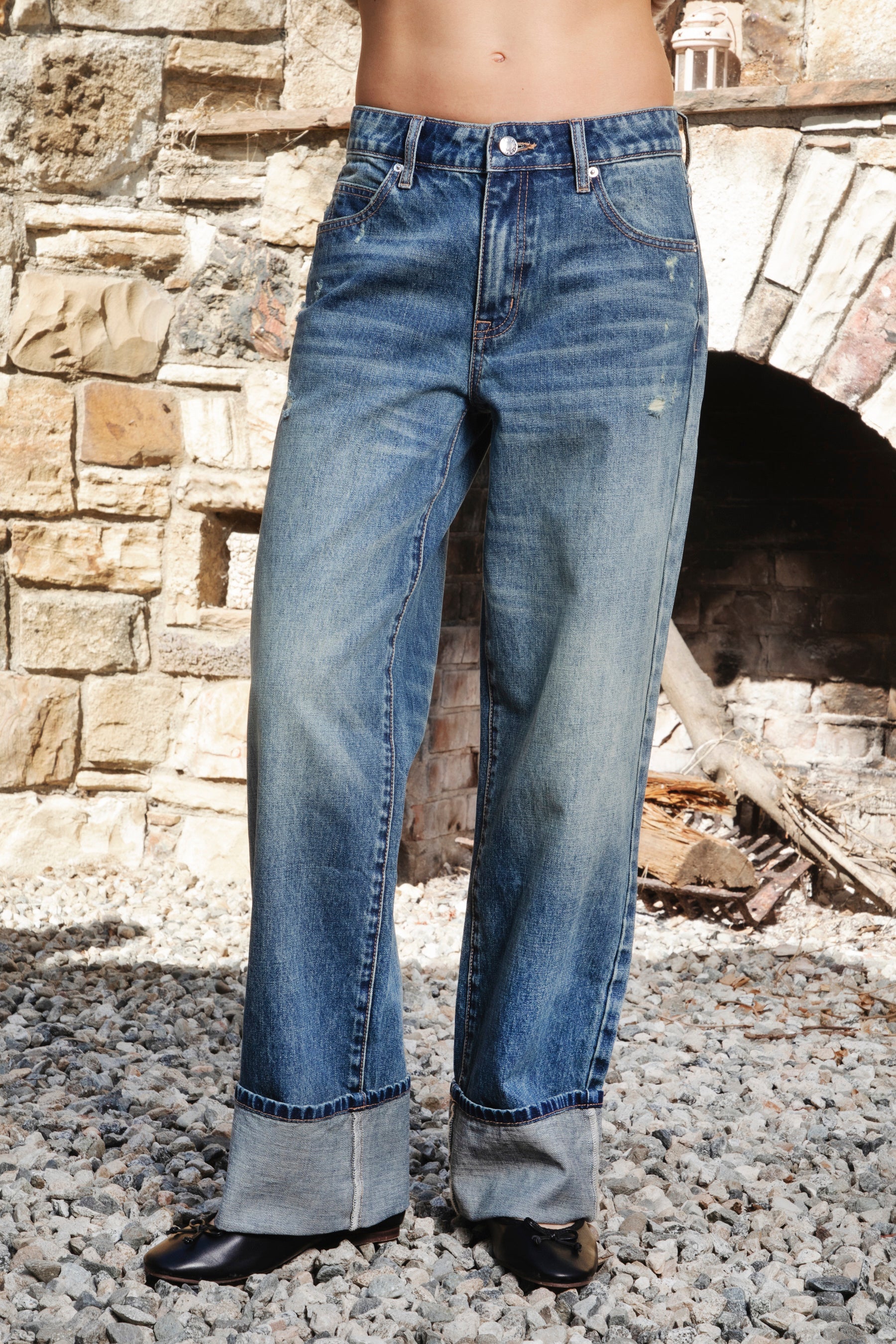 Woman wearing NEOMIE mid rise washed cuffed wide leg jeans featuring non stretch cotton denim, vintage inspired medium blue wash, subtle fading and whiskering, light distressed details, classic five pocket construction, wide straight leg silhouette, extra wide contrast cuffed hems, and button zip fly closure with belt loops.