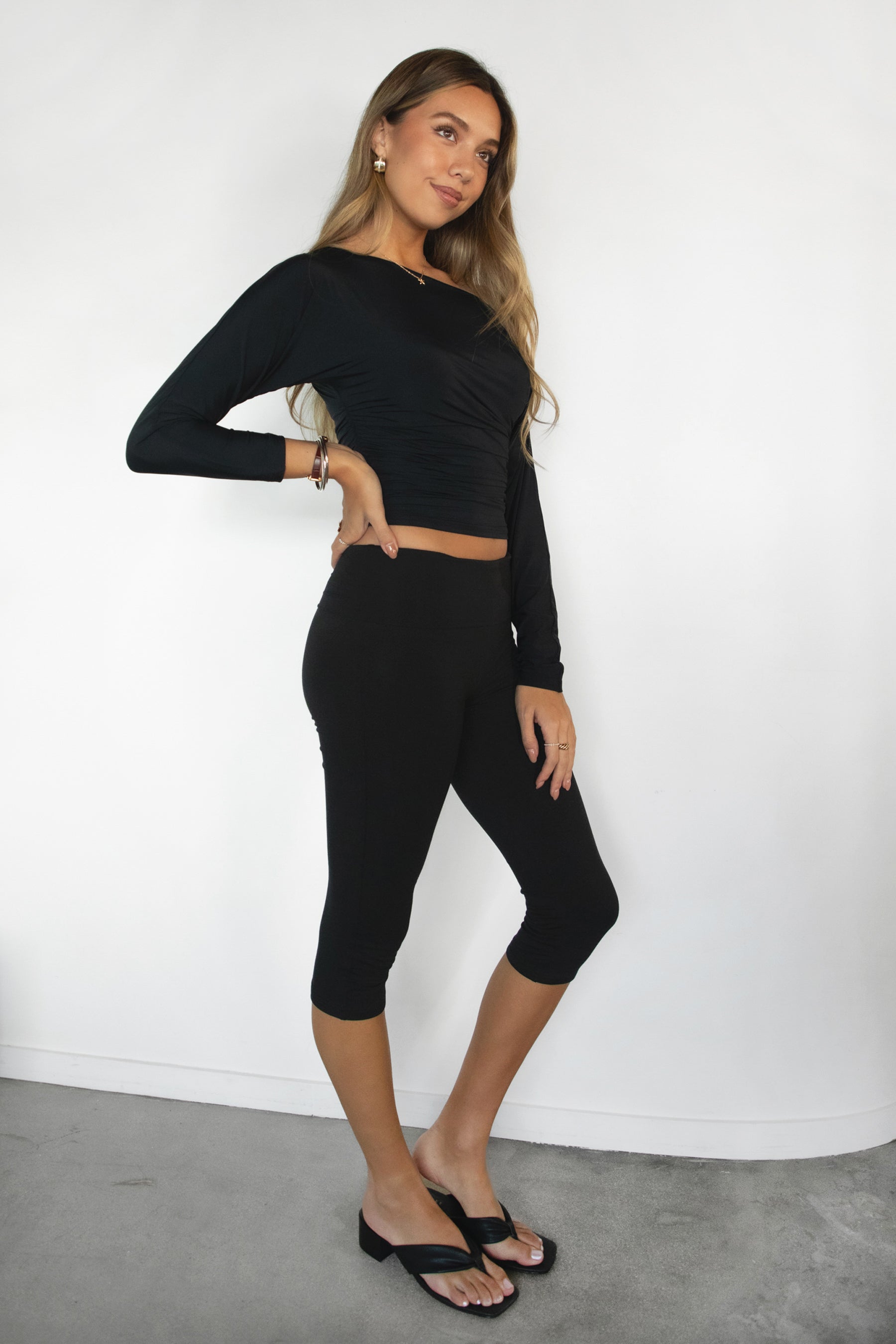 Woman wearing a black long-sleeve top and capri leggings against a white background
