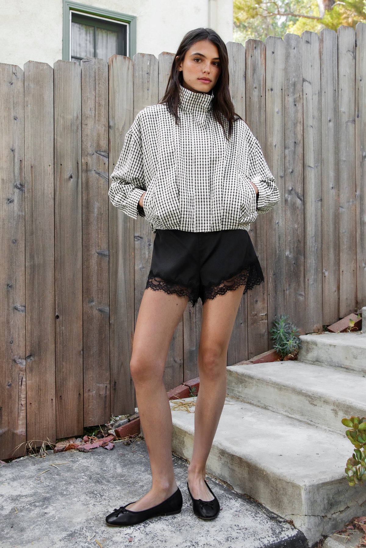 Woman wearing LUNETTE scalloped eyelash lace trim satin shorts IN BLACK featuring soft stretch satin fabric, high rise waist, clean tailored finish, delicate scalloped eyelash lace trim along the hem, hidden back zipper closure, and fully lined interior for added comfort and coverage.