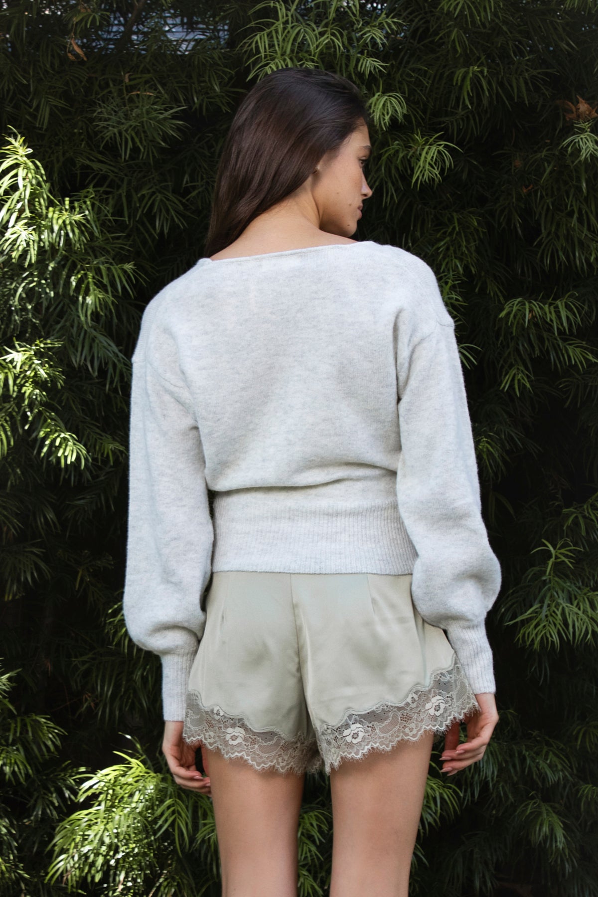 Woman wearing LUNETTE scalloped eyelash lace trim satin shorts IN SAGE featuring soft stretch satin fabric, high rise waist, clean tailored finish, delicate scalloped eyelash lace trim along the hem, hidden back zipper closure, and fully lined interior for added comfort and coverage.