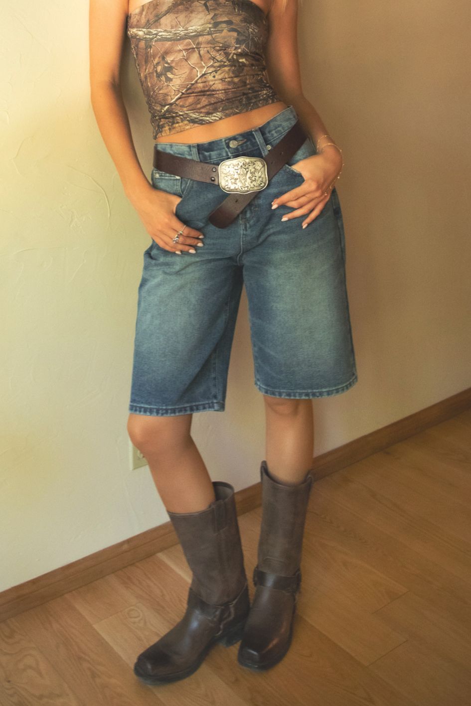 Person wearing a camouflage top, denim shorts, and brown boots indoors.