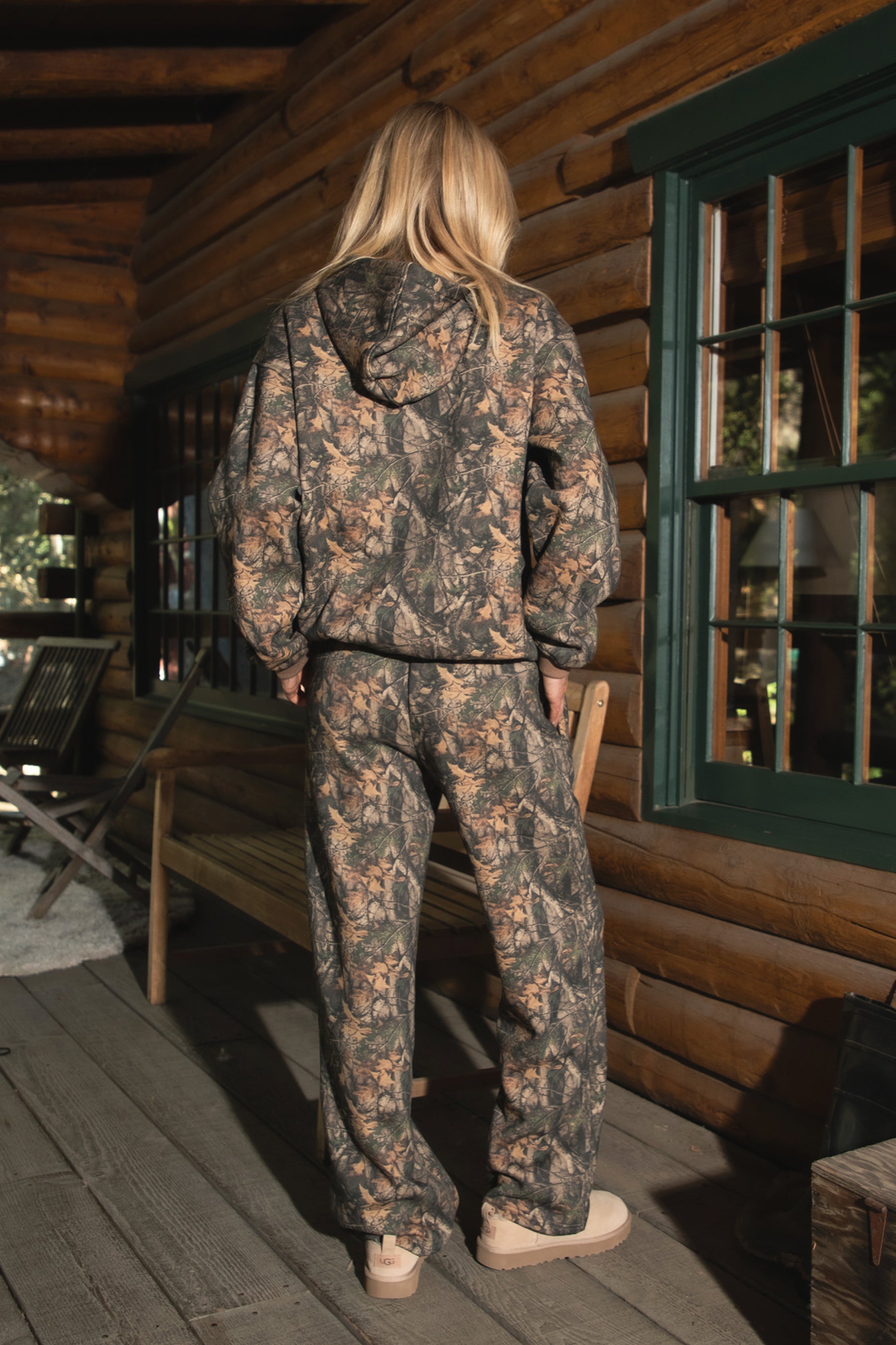 Woman wearing TIC TOC BAYOU Dark Woodland Camo Fleece Wide Leg Sweatpants with deep side pockets, drawcord waist, and drapey Cloud Fleece fabric with matching top on a wooden porch