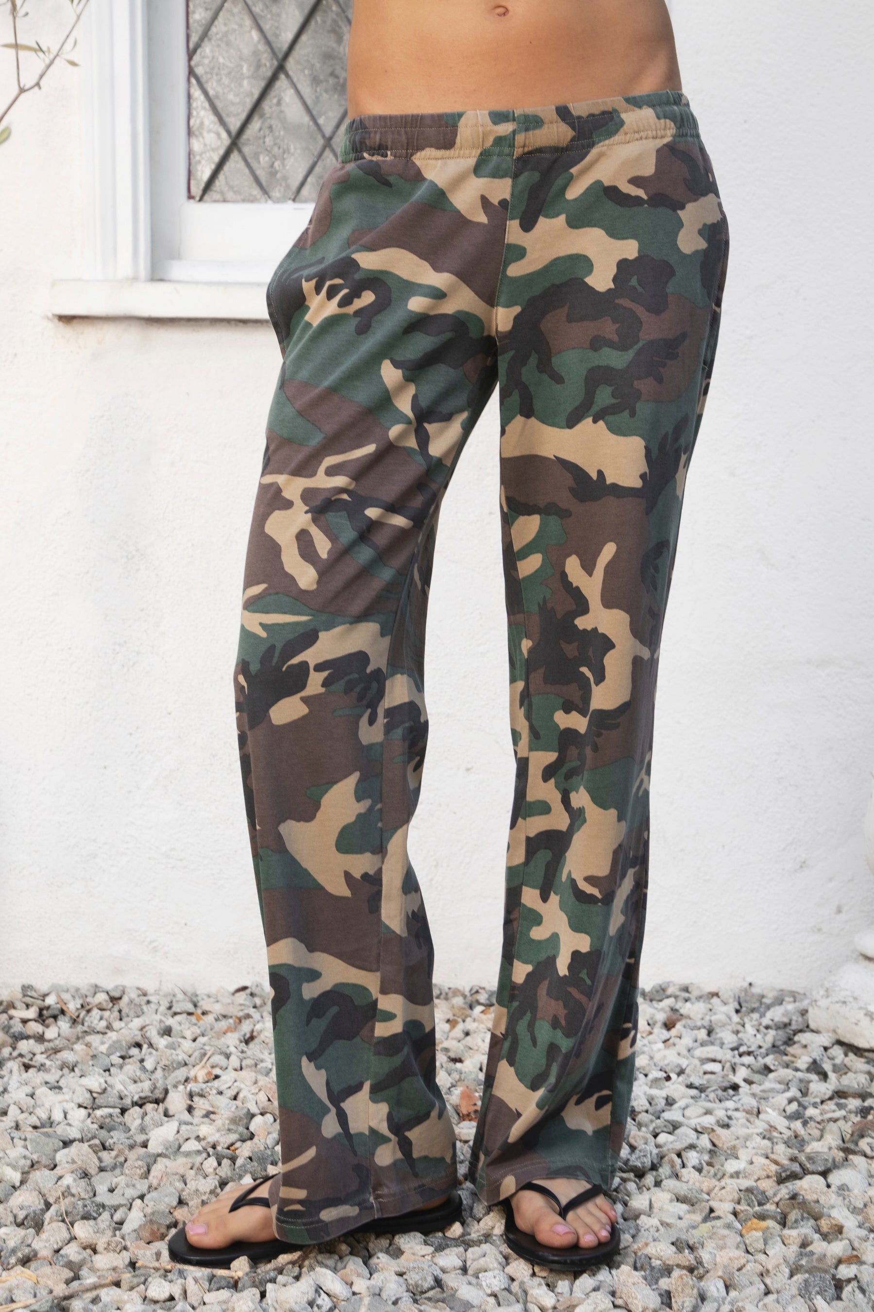 Woman wearing SCOUT military camo washed jersey wide leg pants featuring soft washed cotton jersey fabric, allover classic military camouflage print, comfortable elastic waistband, relaxed straight leg silhouette, functional side pockets, and full length design for laid back casual styling.