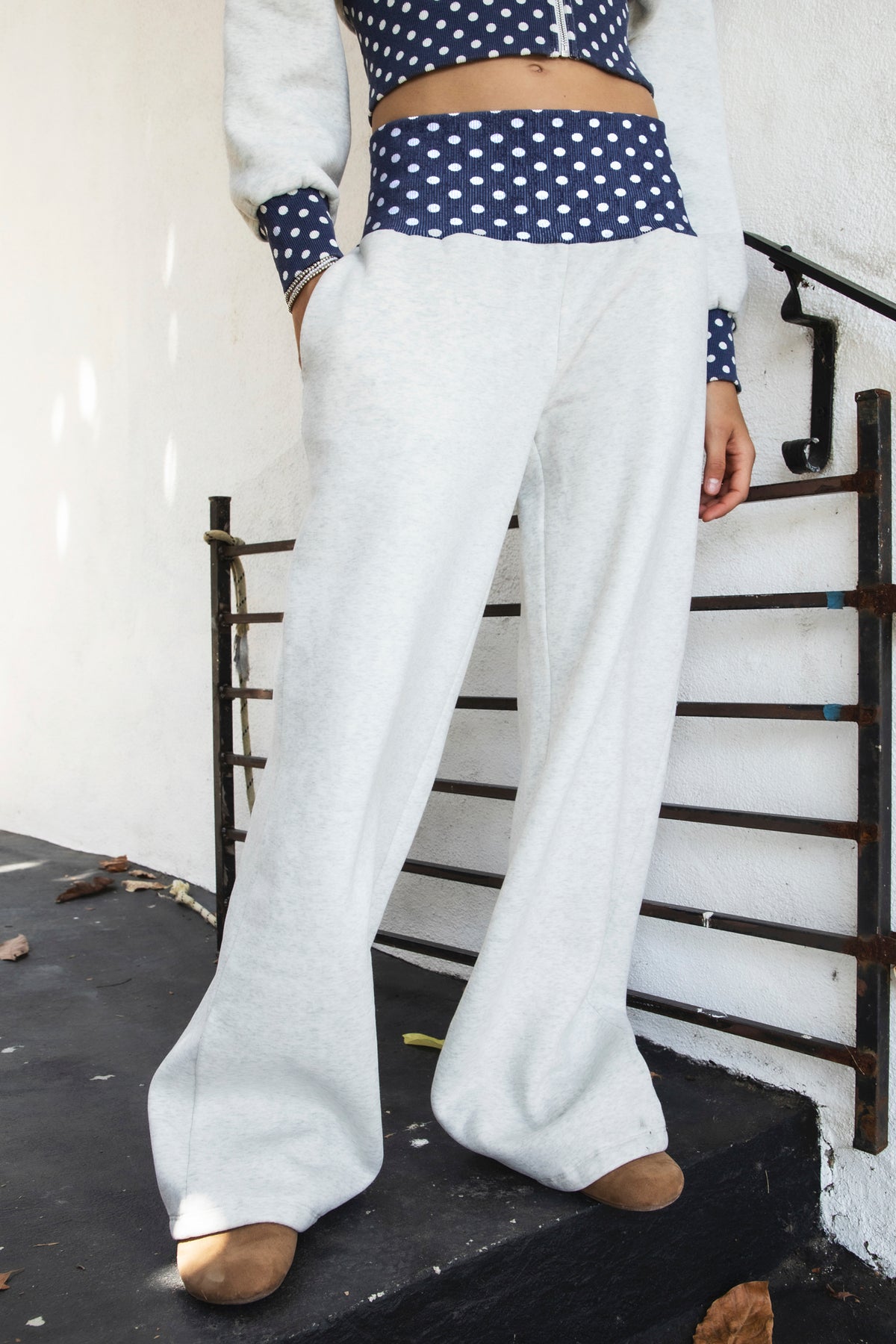 Woman wearing COSETTE polka dot waist wide leg sweatpants featuring soft fleece fabric, relaxed wide leg silhouette, contrast navy ribbed waistband with allover white polka dot pattern, high rise statement fit, soft heather grey body, full length design, functional side pockets, and matching set styling.