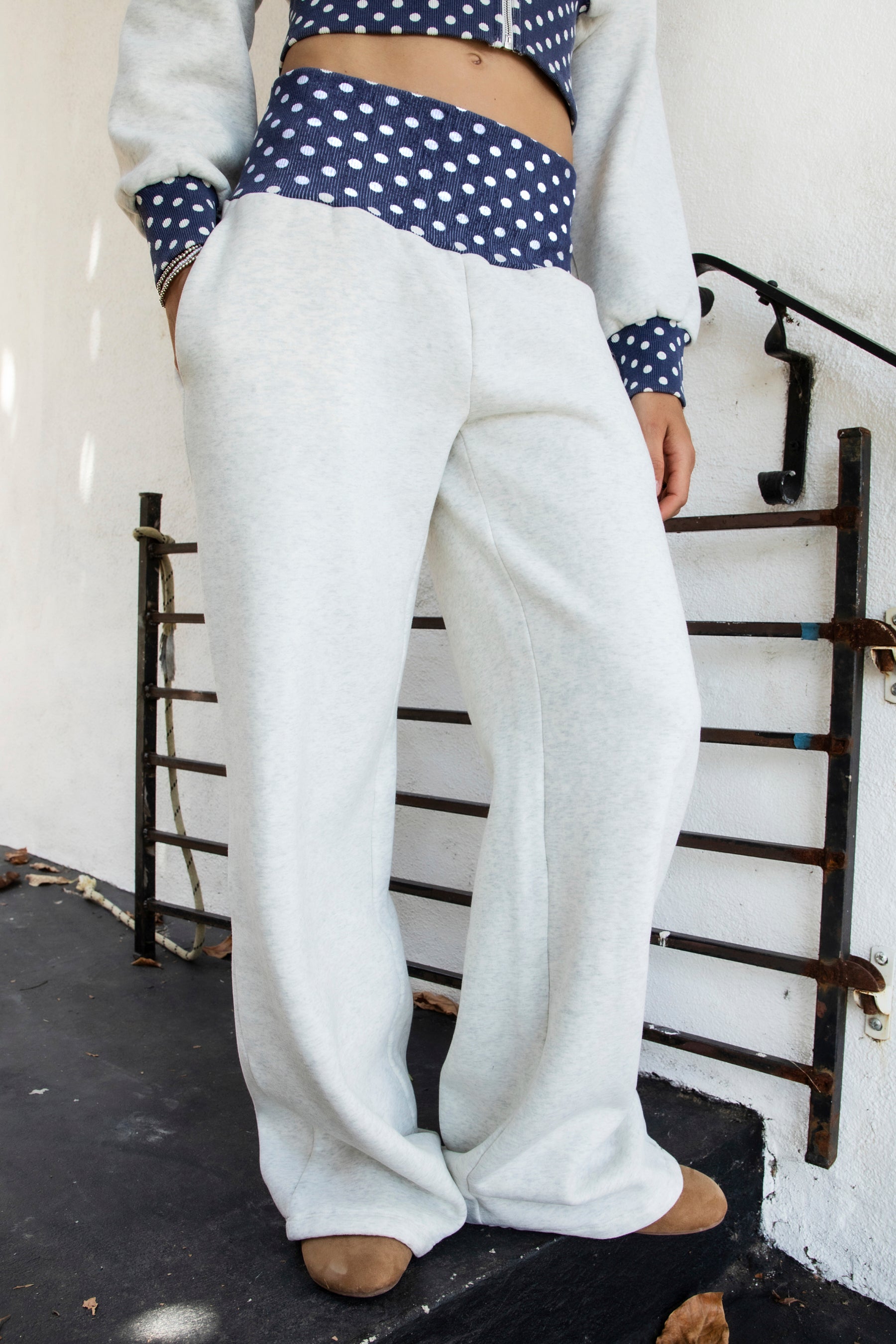 Woman wearing COSETTE polka dot waist wide leg sweatpants featuring soft fleece fabric, relaxed wide leg silhouette, contrast navy ribbed waistband with allover white polka dot pattern, high rise statement fit, soft heather grey body, full length design, functional side pockets, and matching set styling.