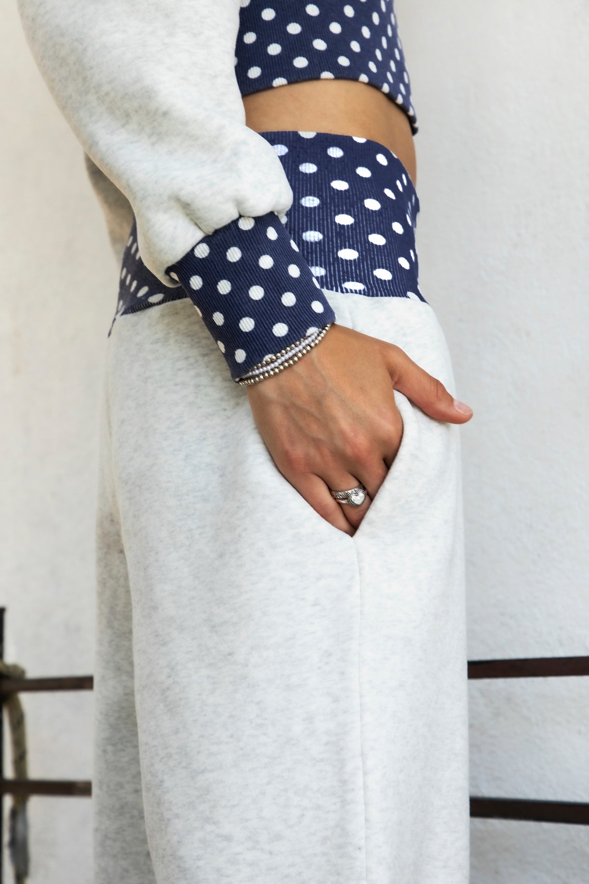 Woman wearing COSETTE polka dot waist wide leg sweatpants featuring soft fleece fabric, relaxed wide leg silhouette, contrast navy ribbed waistband with allover white polka dot pattern, high rise statement fit, soft heather grey body, full length design, functional side pockets, and matching set styling.