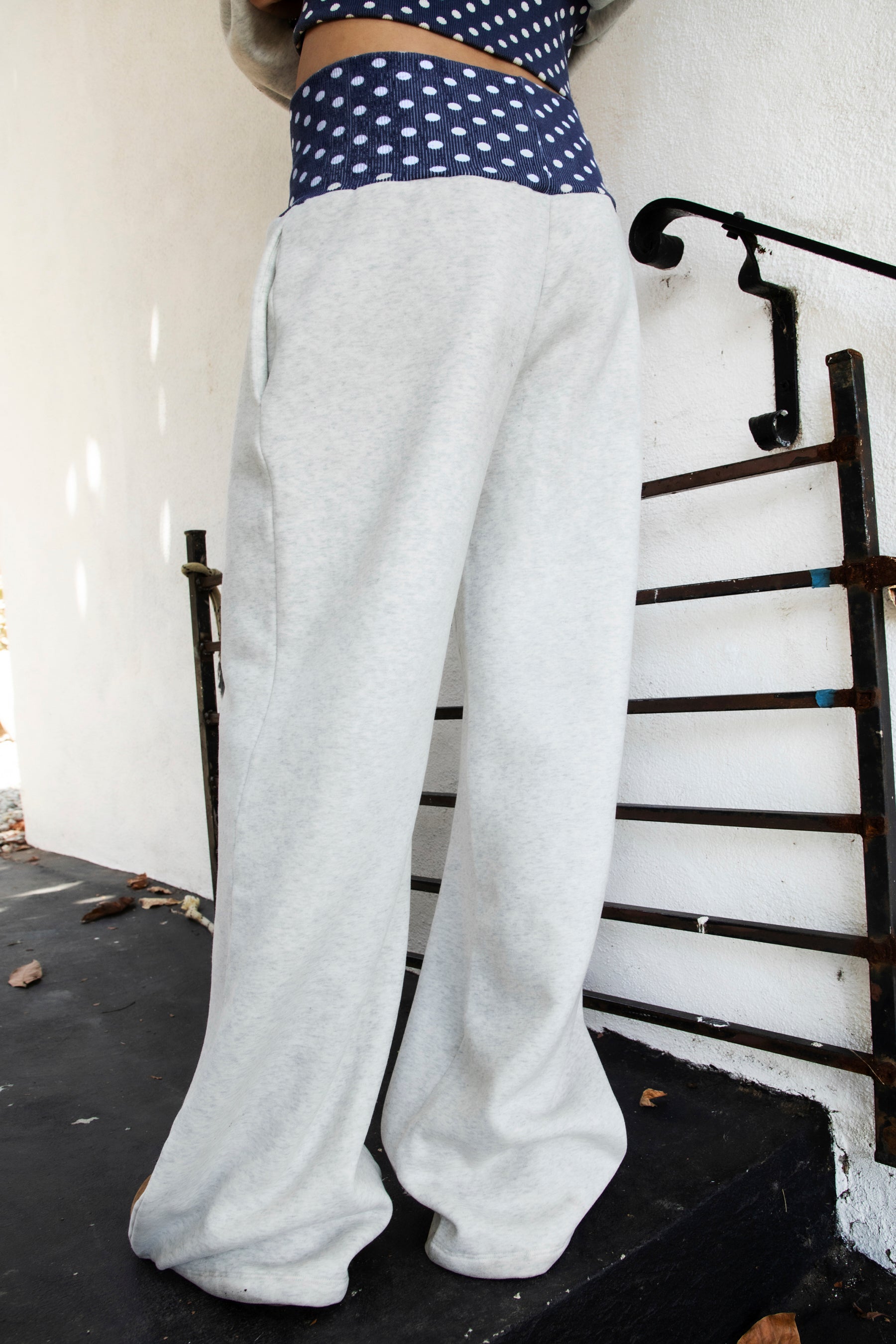 Woman wearing COSETTE polka dot waist wide leg sweatpants featuring soft fleece fabric, relaxed wide leg silhouette, contrast navy ribbed waistband with allover white polka dot pattern, high rise statement fit, soft heather grey body, full length design, functional side pockets, and matching set styling.