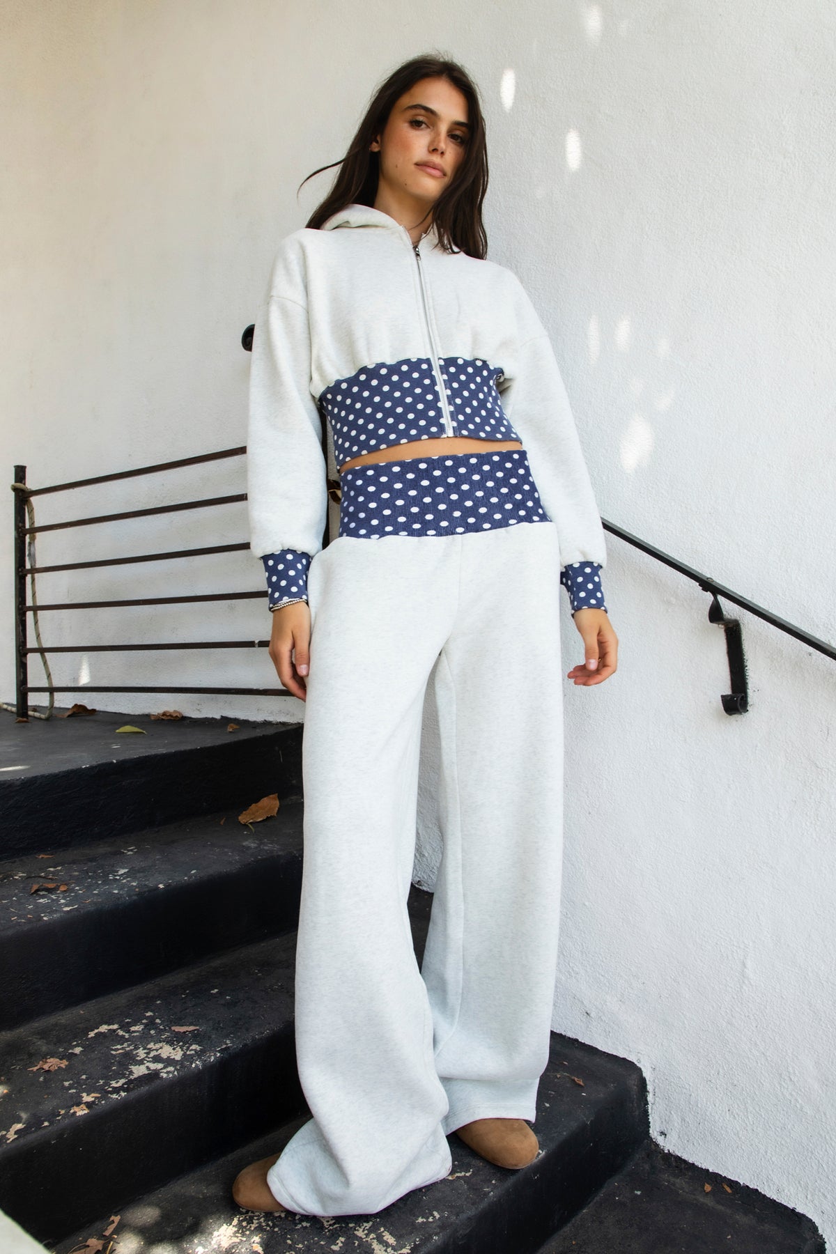 Woman wearing COSETTE polka dot waist wide leg sweatpants featuring soft fleece fabric, relaxed wide leg silhouette, contrast navy ribbed waistband with allover white polka dot pattern, high rise statement fit, soft heather grey body, full length design, functional side pockets, and matching set styling.