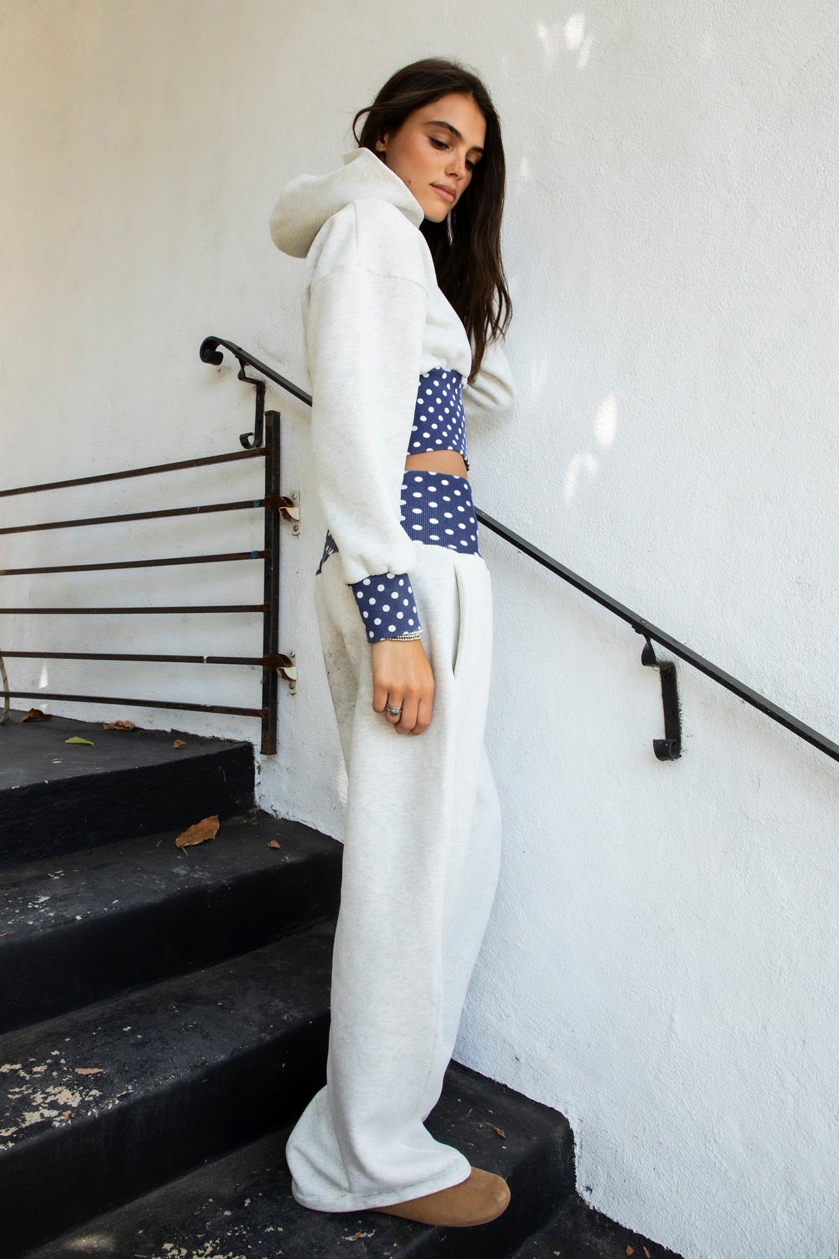 Woman wearing COSETTE polka dot waist wide leg sweatpants featuring soft fleece fabric, relaxed wide leg silhouette, contrast navy ribbed waistband with allover white polka dot pattern, high rise statement fit, soft heather grey body, full length design, functional side pockets, and matching set styling.
