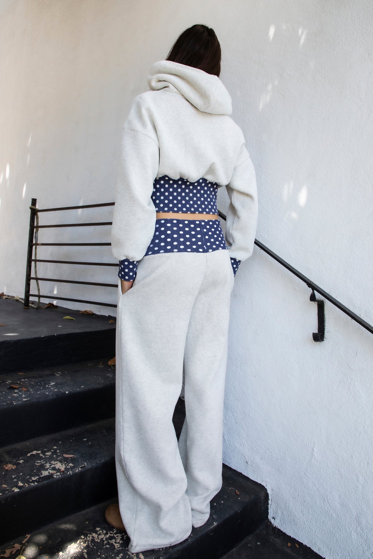 Woman wearing COSETTE polka dot waist wide leg sweatpants featuring soft fleece fabric, relaxed wide leg silhouette, contrast navy ribbed waistband with allover white polka dot pattern, high rise statement fit, soft heather grey body, full length design, functional side pockets, and matching set styling.
