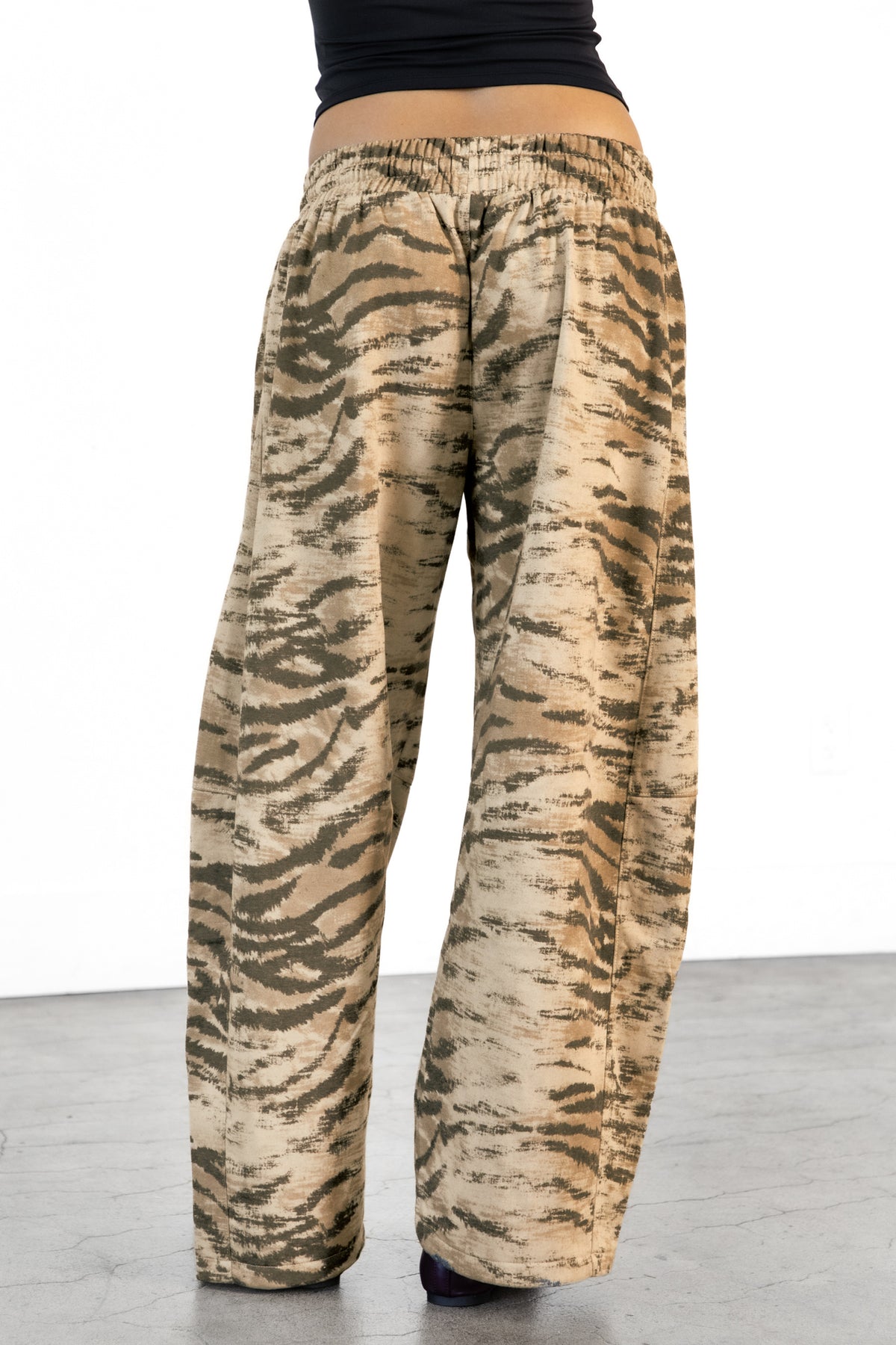 Woman wearing ZARIA tiger print wide leg pants featuring soft polyester cotton blend fabric, allover abstract tiger print in earthy beige, brown, and olive tones, elastic waistband with adjustable drawstring tie, relaxed fit through the hips and thighs, functional side pockets, wide leg silhouette with a subtle barrel shape, and full length design with paneled seam detailing.
